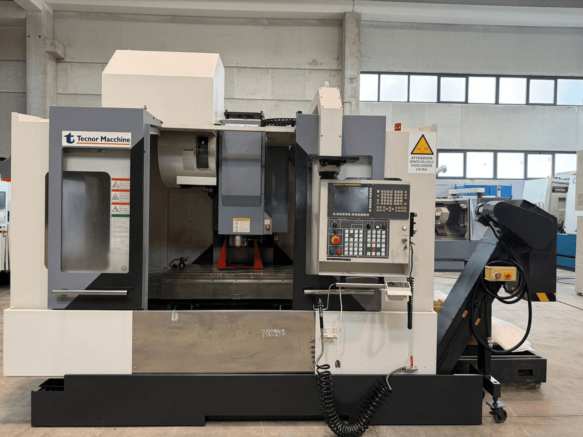 Tecnor Machine CNC frēzmašīnas priekšējais skats, vadības panelis ar pogām, brīdinājuma uzlīmes un instrumentu turētājs.