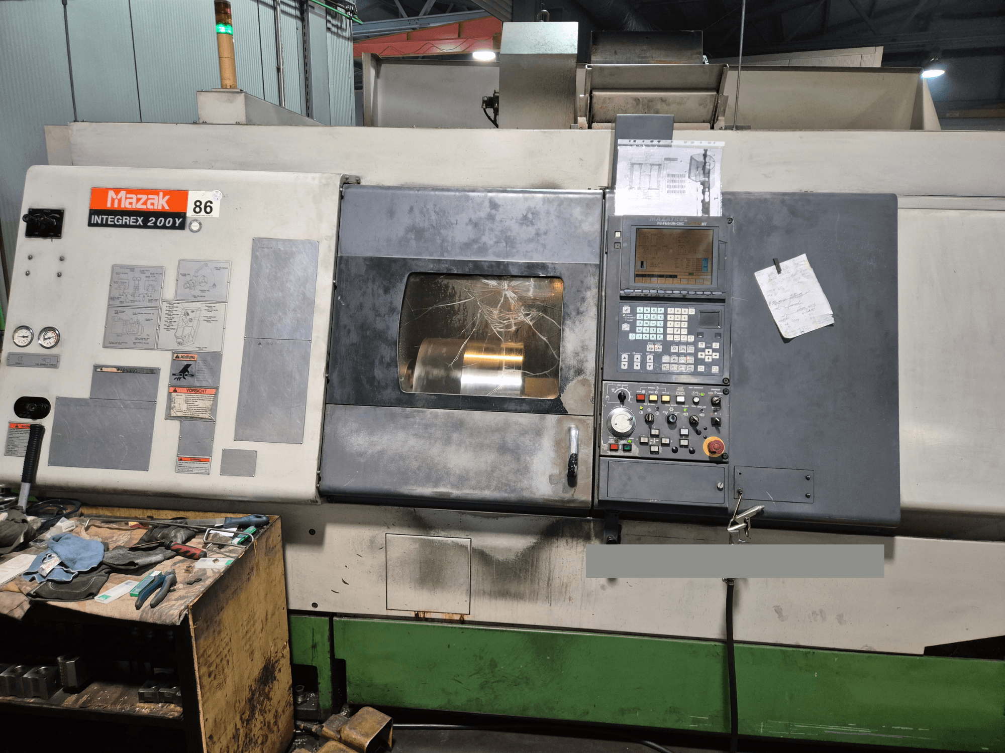 Mazak Integrex 200Y virpmašīna, skats no priekšpuses, ar vadības paneli un instrumentiem uz darbgalda. Redzami mērinstrumenti un displeja ekrāns.