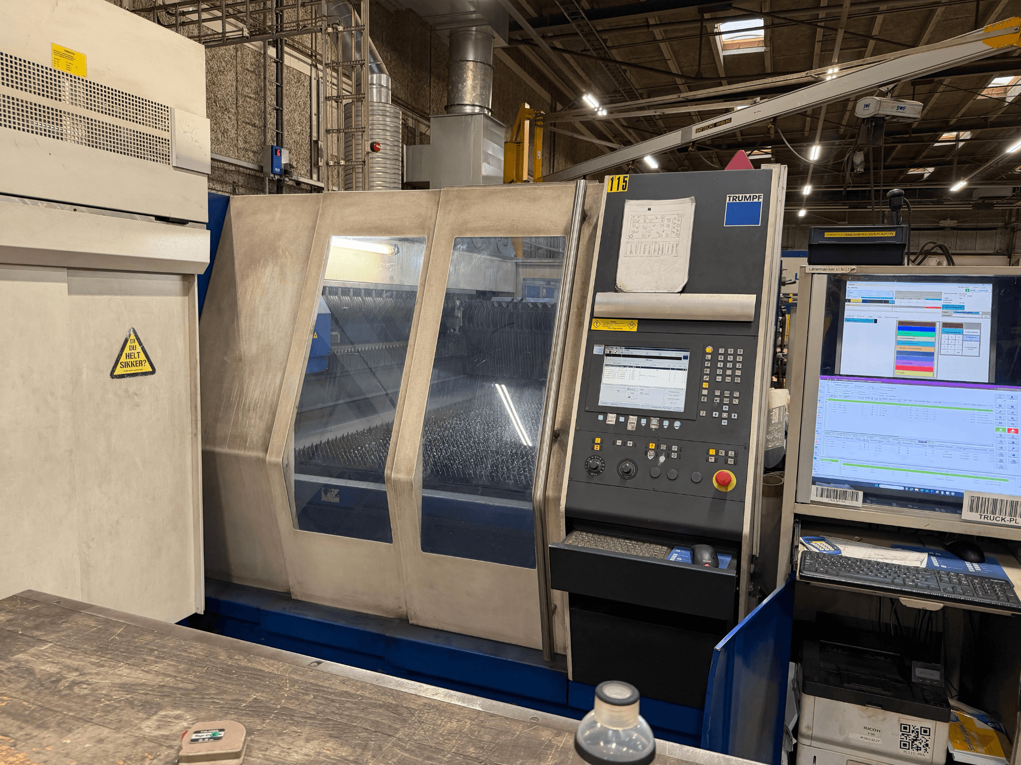 Rūpnīcas vidē uzstādīta Trumpf rūpnieciskā lāzera iekārta ar vadības paneli un digitālajiem displejiem.