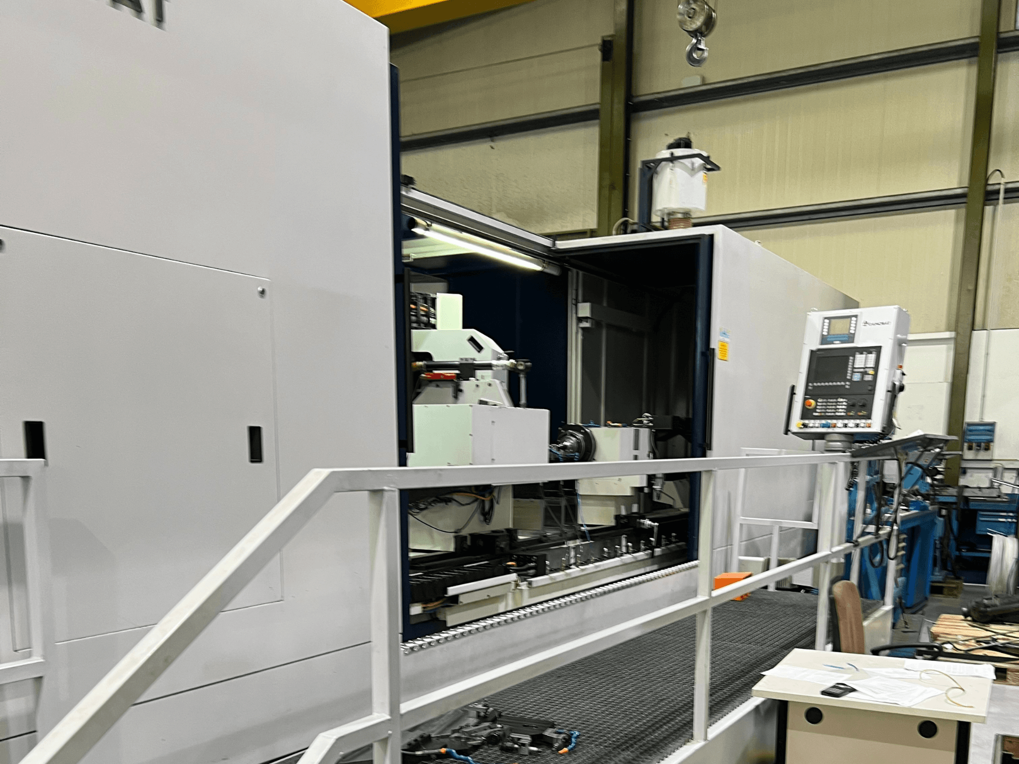 CNC apstrādes centrs ar atvērtu sānu skatu, kurā redzamas vadības ierīces, instrumentu turētājs un galvenā detaļa iekšpusē. Zīmola detaļas nav redzamas.