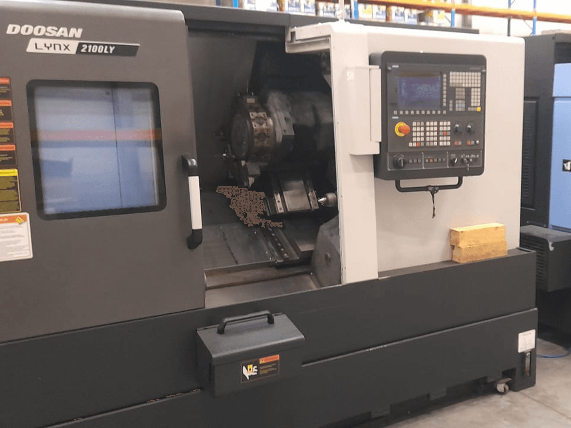 Doosan Lynx 2100LY CNC virpa, priekšējais skats, kurā redzams vadības panelis, instrumentu turētājs un iekšējā darba telpa; redzamas tehniskās etiķetes.