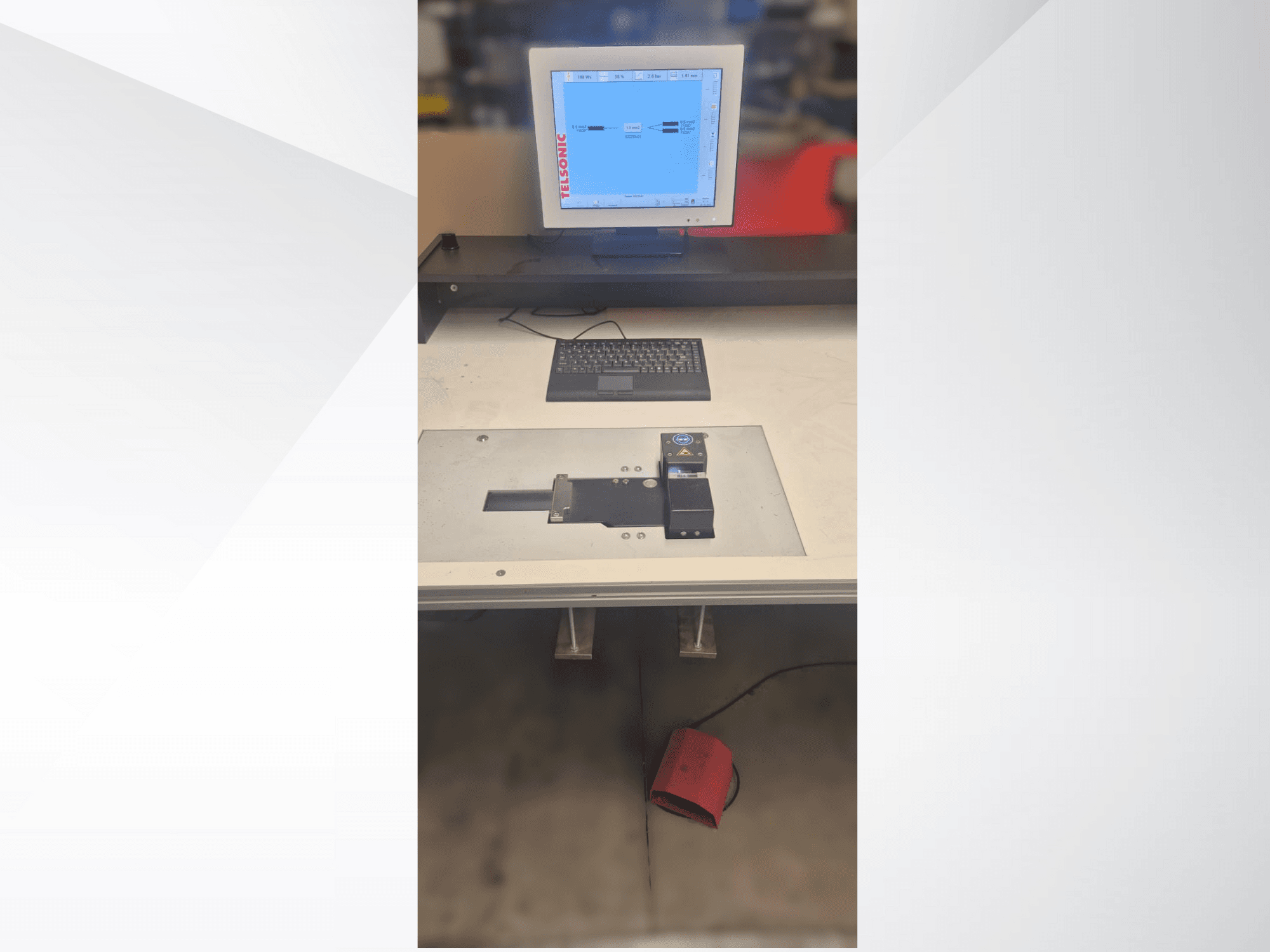 Testēšanas stacijas skats no augšas uz leju ar datora monitoru, tastatūru un vadības paneli ar pogu un zaļu gaismu.