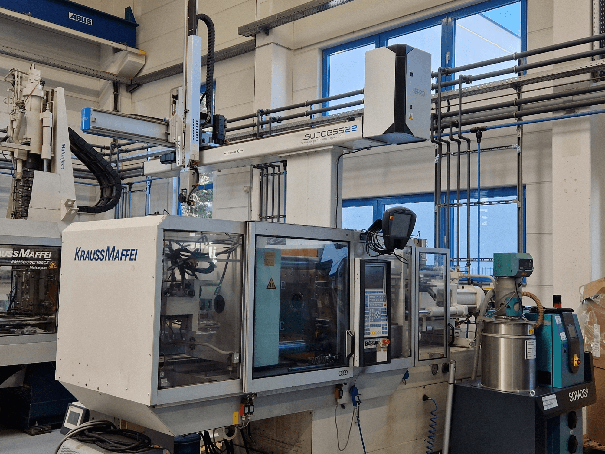 KraussMaffei Success 22 iesmidzināšanas veidošanas iekārta ar vadības paneli, skatīts no priekšpuses rūpnīcā.