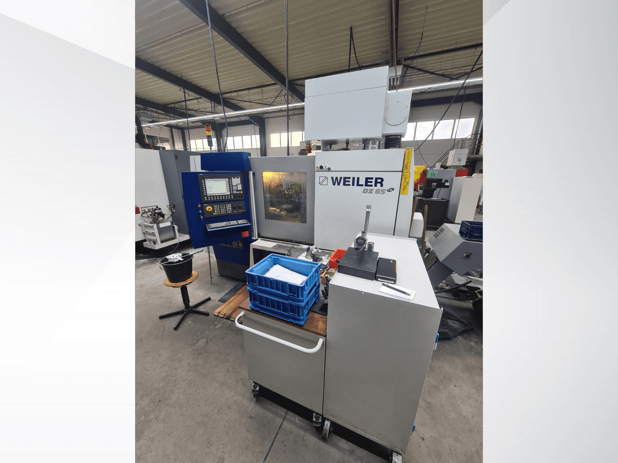 Weiler DZ 65 CNC darbnīcā, skats no priekšpuses ar vadības paneli, instrumentiem un zilajiem glabāšanas nodalījumiem.