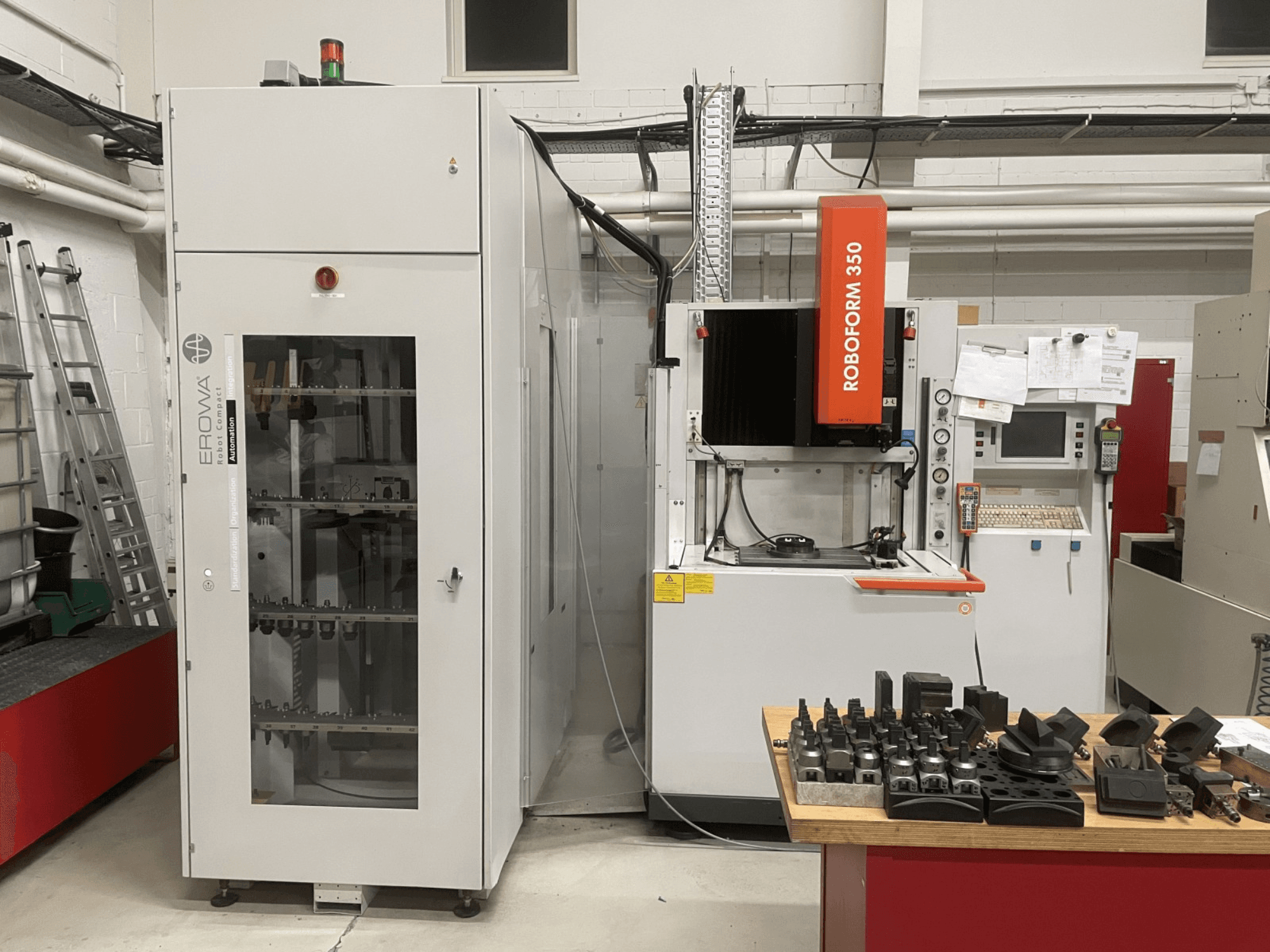 Caurumošanas EDM mašīna CHARMILLES Roboform 350, skats no priekšpuses, ar instrumentiem uz galda un blakus esošajām iekārtām.