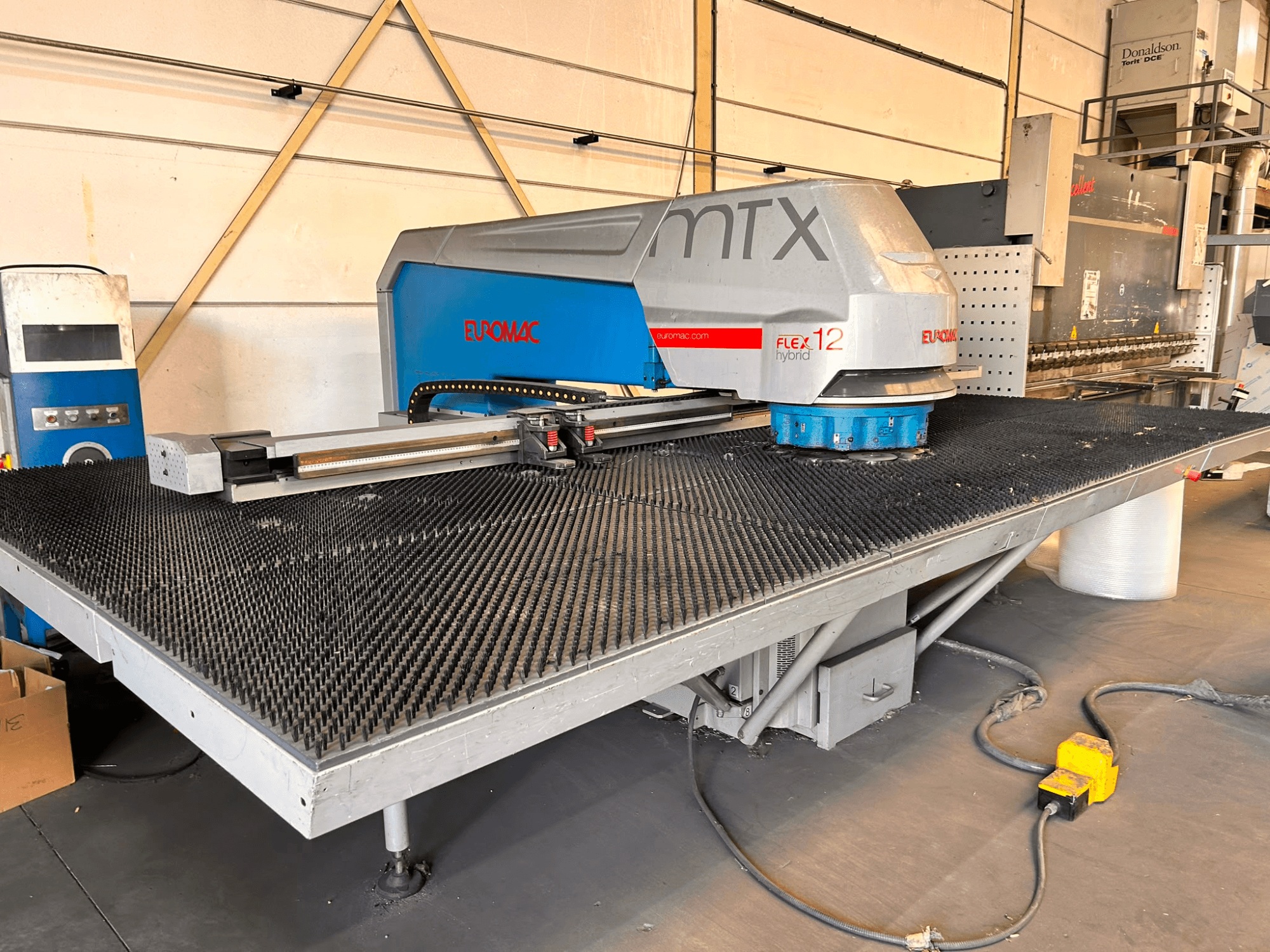Euromac MTX FLEX 12 CNC perforācijas mašīna, skats no priekšpuses, ar lielu perforētu galdu un vadības paneli.