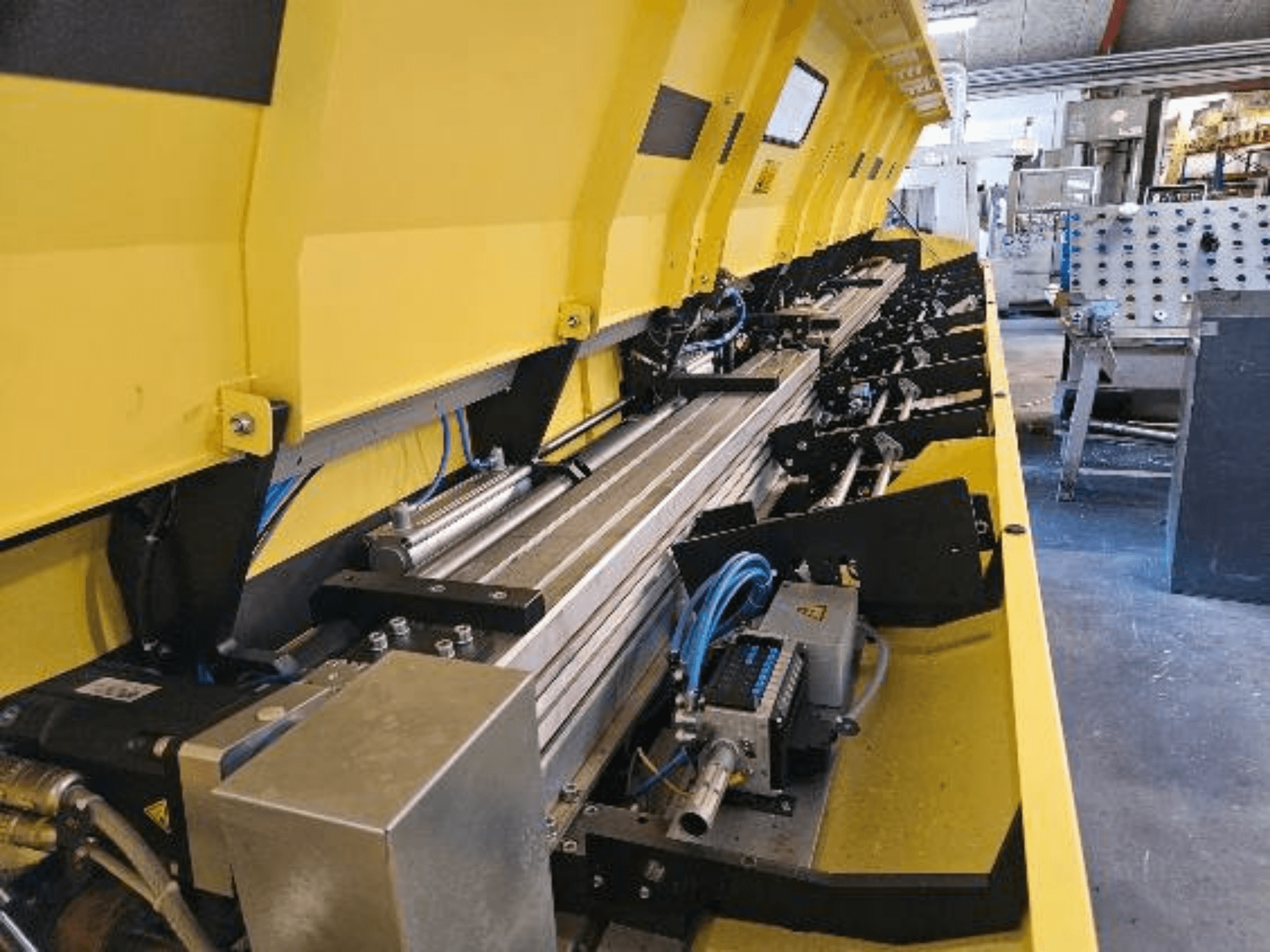 Skats tuvplānā uz dzeltenu hidraulisko mašīnu ar metāla detaļām un konveijera sliedēm, šļūtenēm un elektroniskām detaļām.