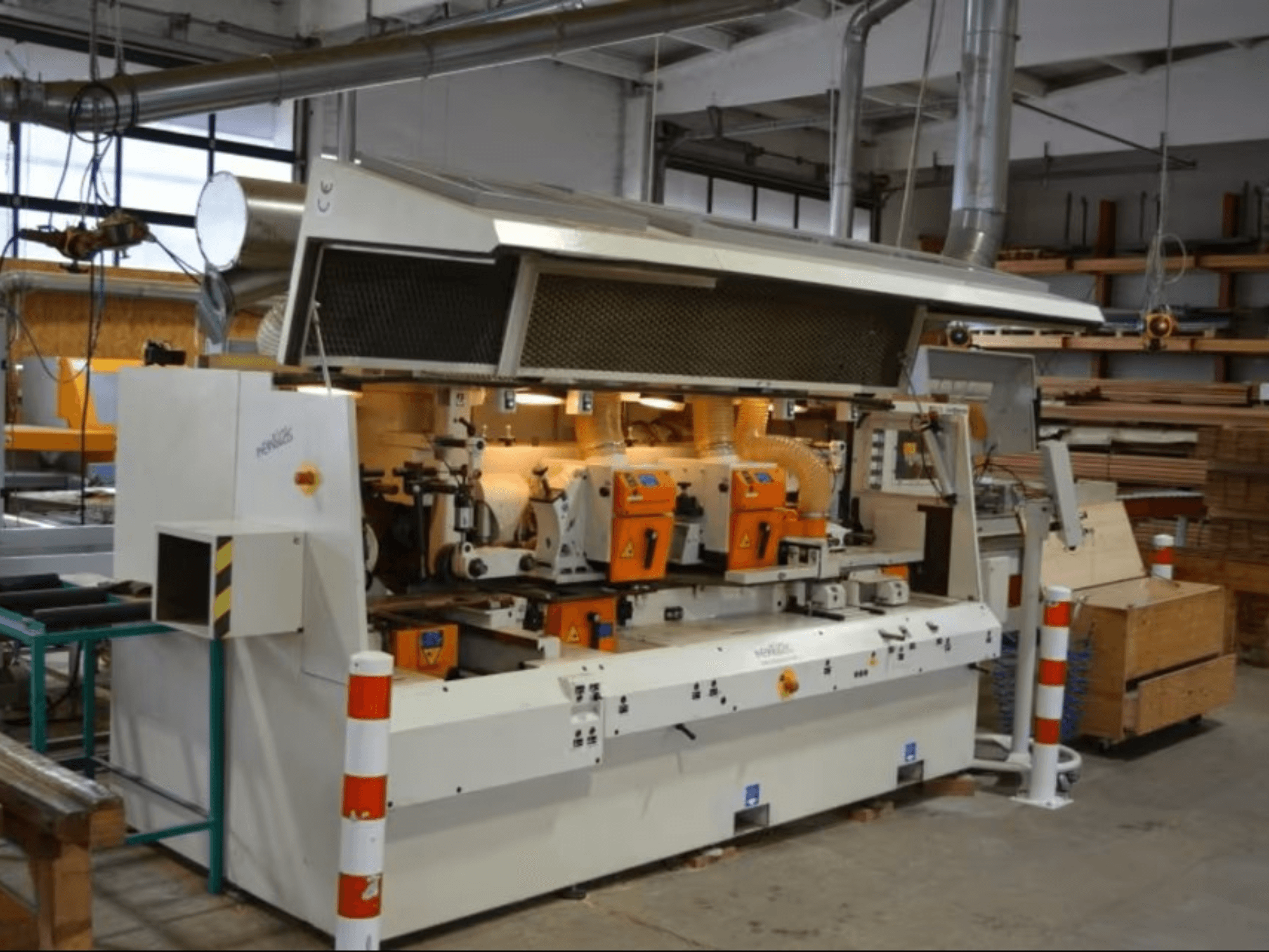 Kokapstrādes mašīna PENIGAS, skats no priekšpuses, ar divām oranžām griešanas galviņām un putekļu nosūces sistēmu darbnīcā.