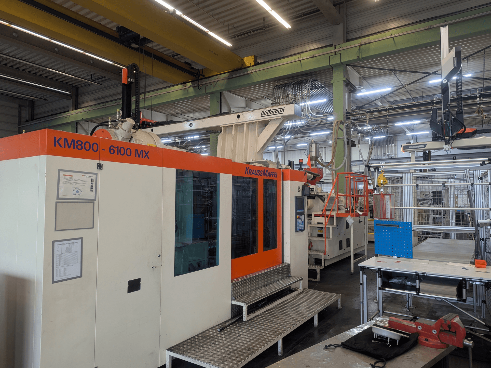 Krauss Maffei KM 800-6100MX hidrauliskā iesmidzināšanas iekārta, skats no priekšpuses, vadības panelis un rūpnieciskā uzstādīšana.