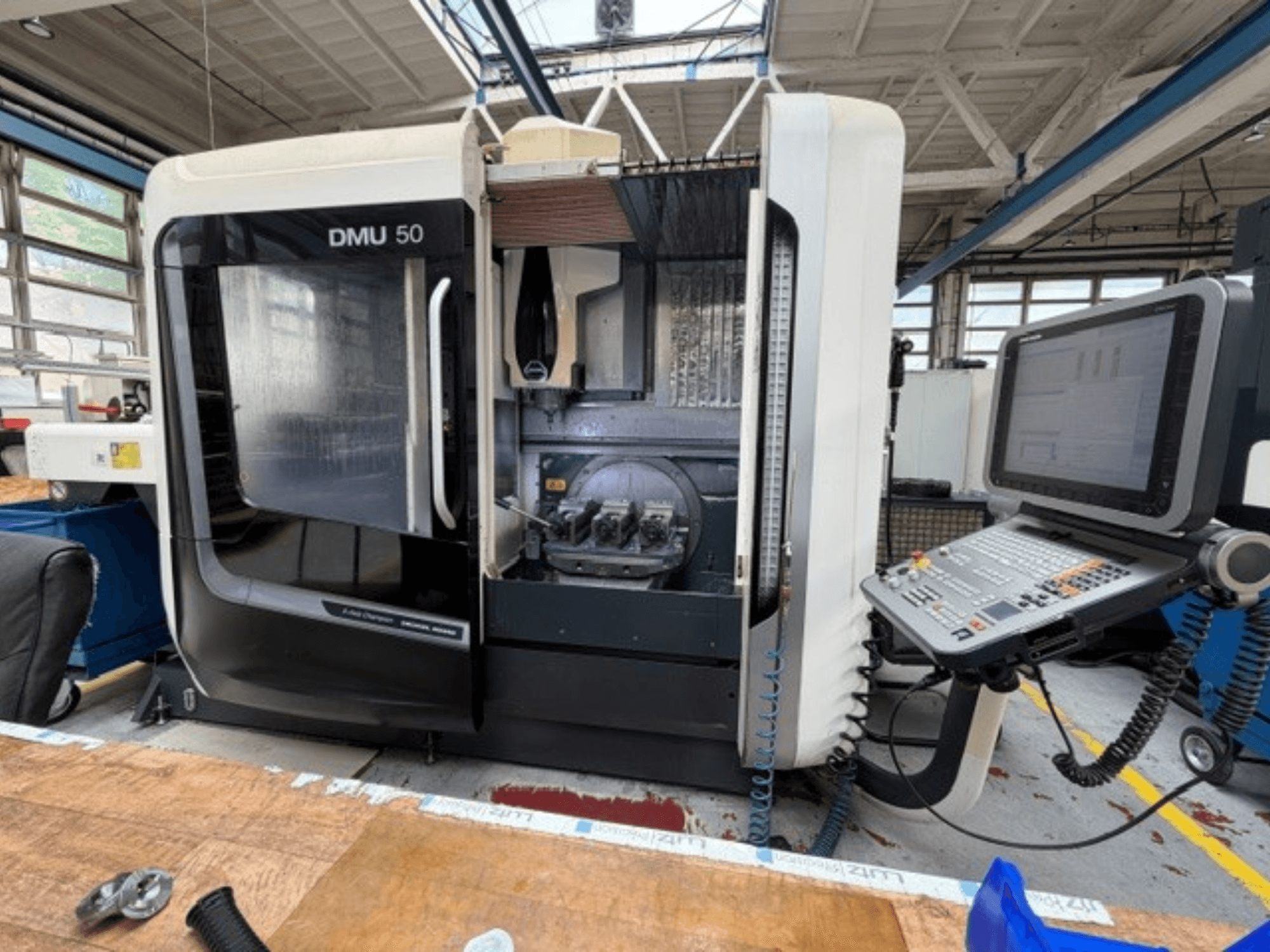 DMG MORI DMU 50 trešās paaudzes vertikālais apstrādes centrs, redzams no priekšpuses, ar atvērtām durvīm, redzams CNC vadības panelis un darba telpa iekšpusē.
