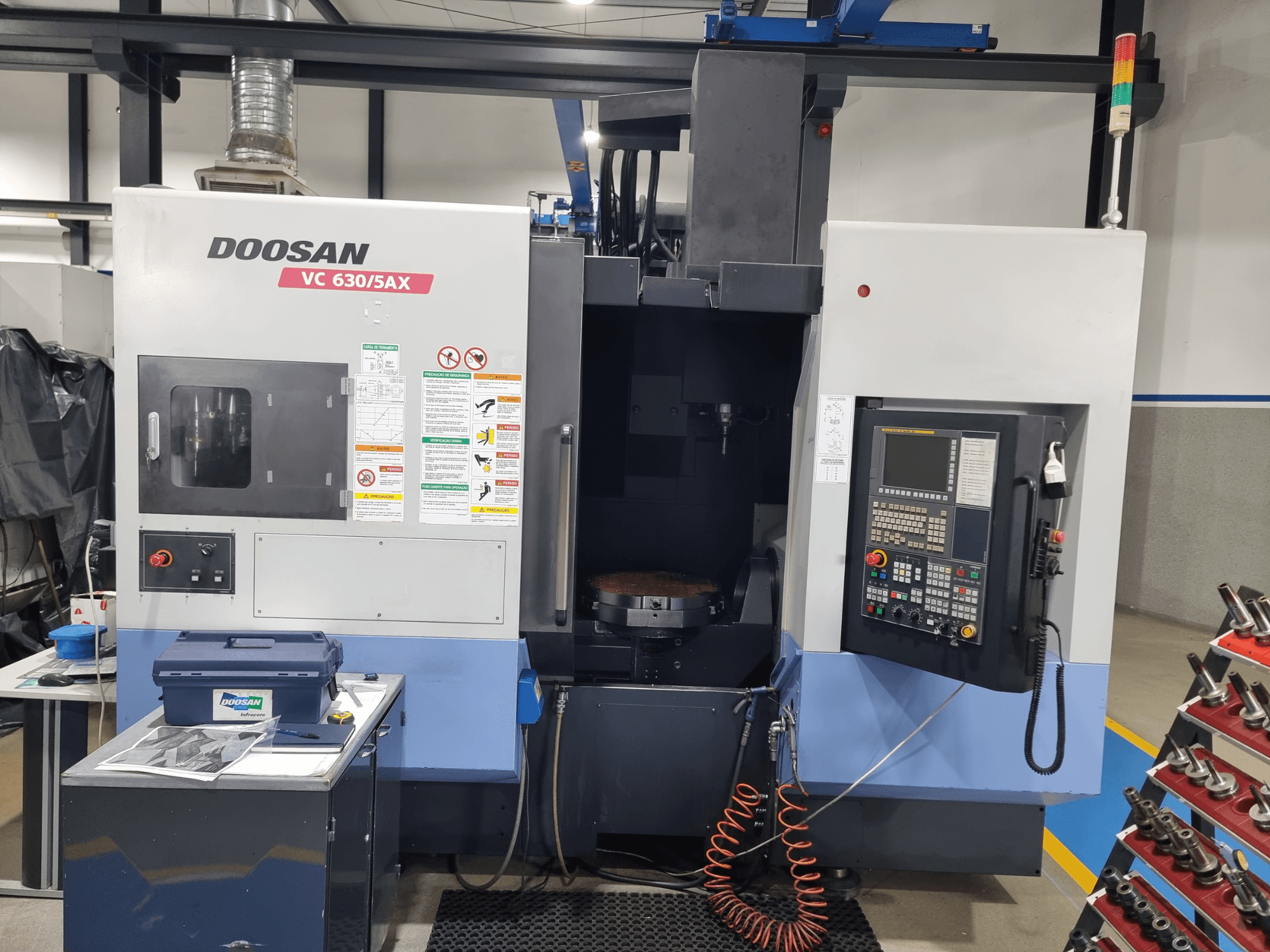 DOOSAN VC 630/5AX universālais apstrādes centrs, skats no priekšpuses, kurā redzams vadības panelis, griešanas zona un drošības elementi.