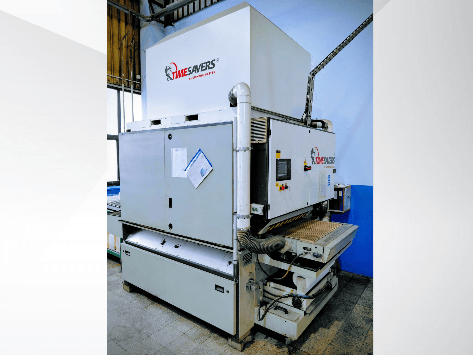 Timesavers rūpnieciskā slīpmašīna, skats no priekšpuses. Aprīkots ar vadības ierīcēm, putekļu nosūcēju un regulējamu slīpēšanas gultni precizitātes nodrošināšanai.