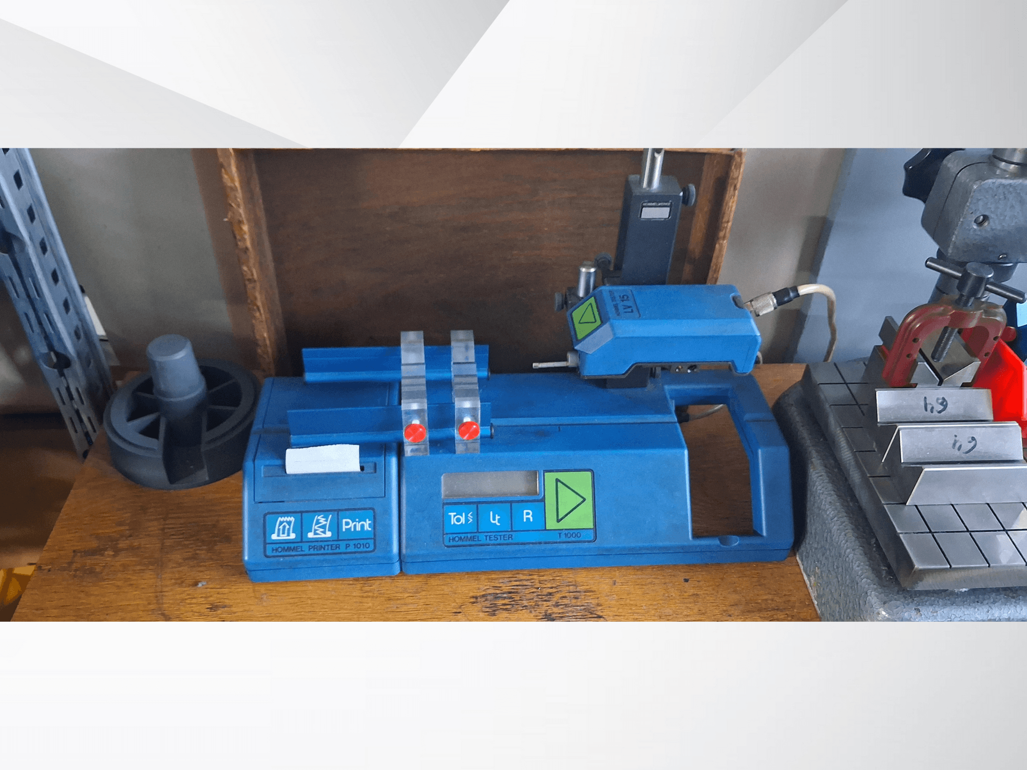 Hommel printeris P 1010 un testeris T1000 sānu skatā, ar zilu korpusu, pogām un sarkaniem indikatoriem uz darba galda.