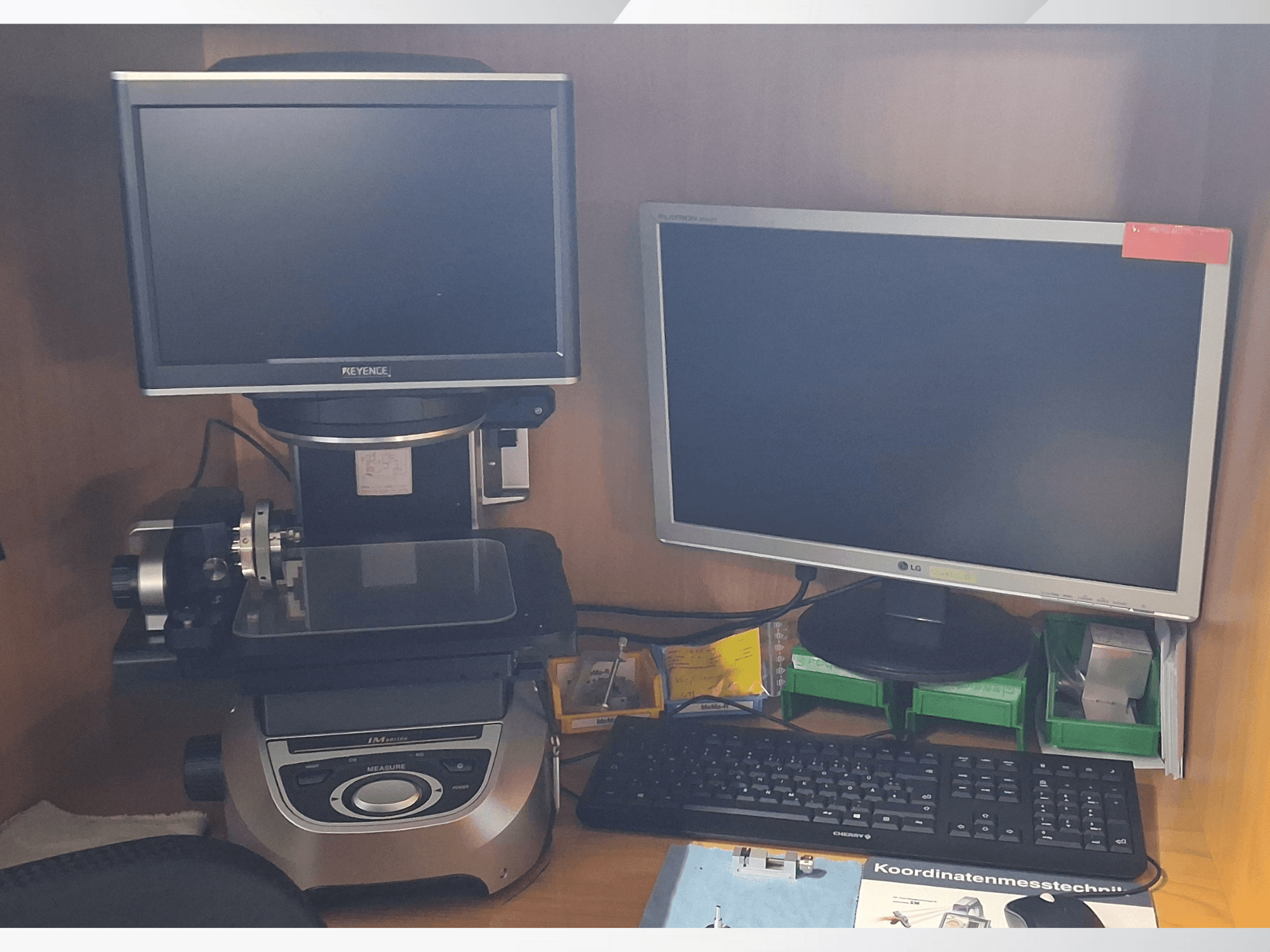 Keyence mērījumu sistēma ar diviem monitoriem (vienu LG, otru Keyence) un tastatūru, skatoties no priekšpuses.