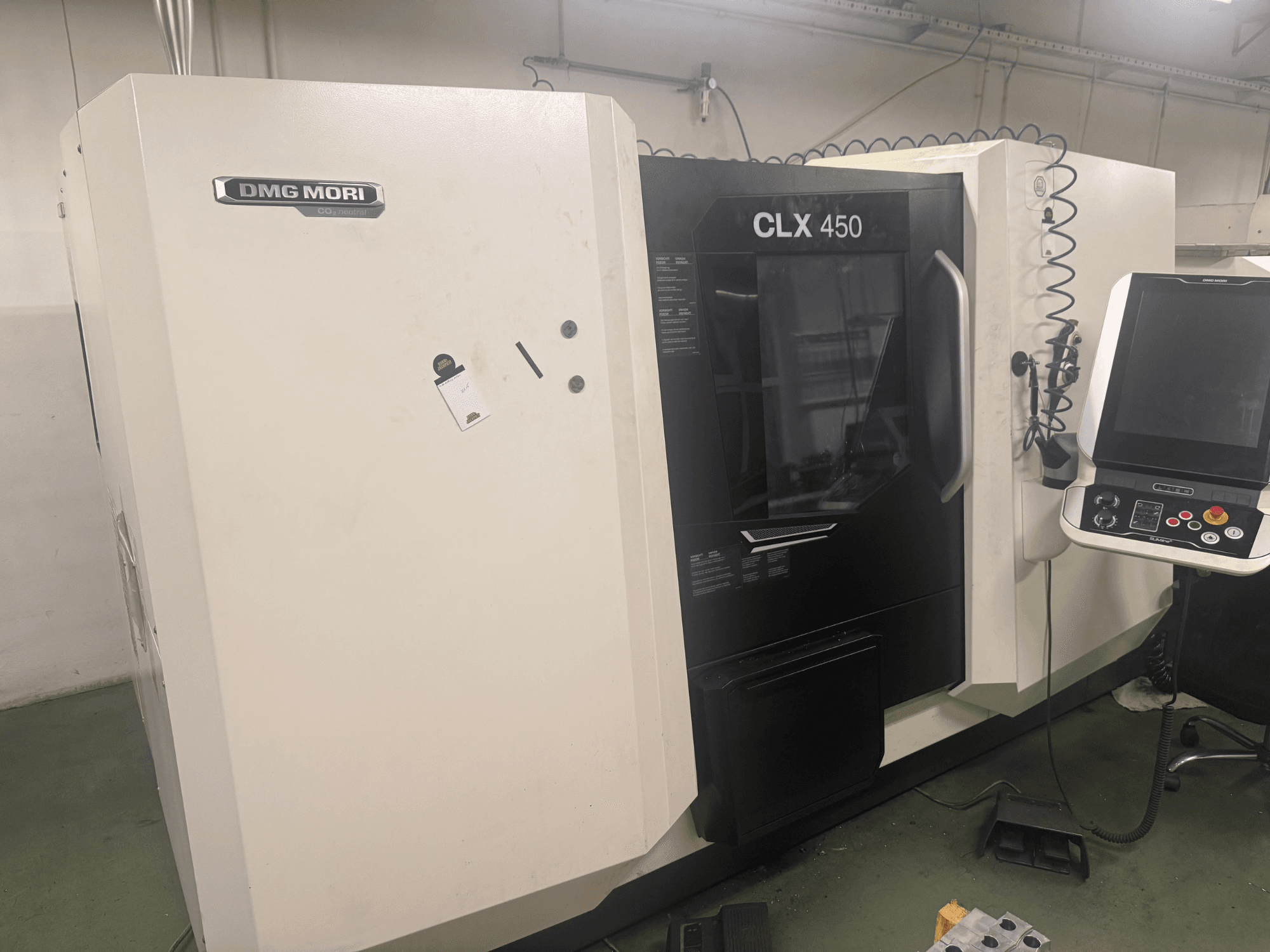 DMG MORI CLX 450 CNC mašīna, skats no sāniem ar vadības paneli, redzamām vadības pogām un tīru darba vietu.