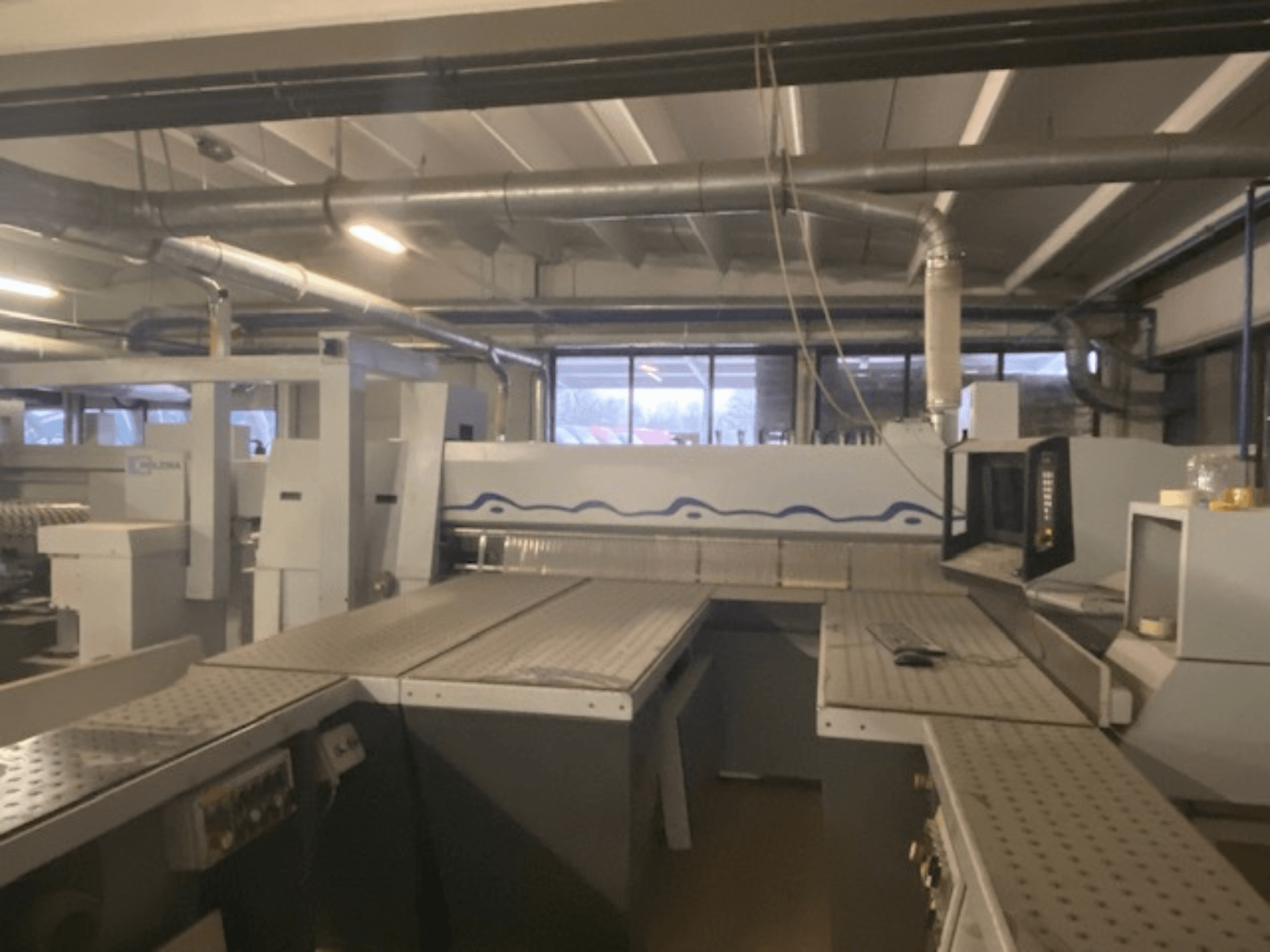 Rūpnieciska darba telpa ar iekārtu komplektu un vadības paneli, skatoties no paaugstināta priekšējā leņķa.