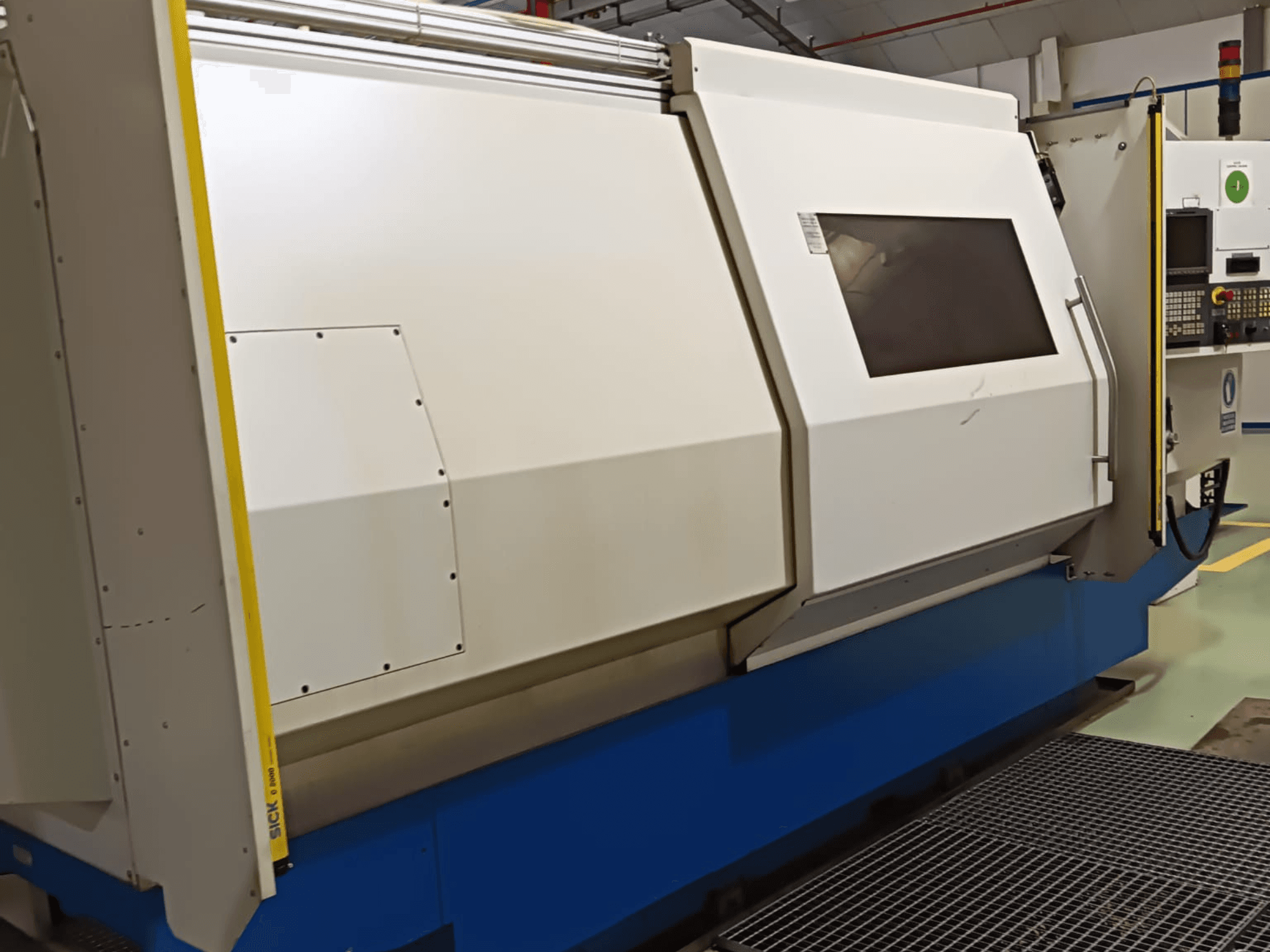 Rūpnieciskās virpas, skats no sāniem, ar lielu balti zilu korpusu, digitālo vadības paneli un drošības funkcijām.