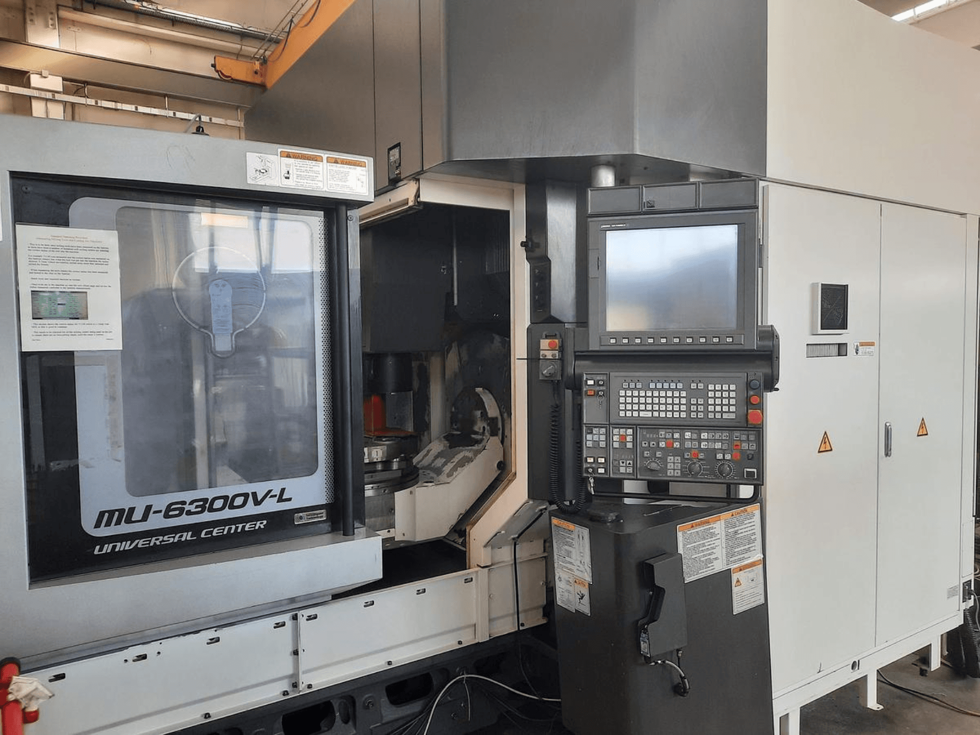 MU-6300V-L universālā centra mašīna no priekšpuses, redzams vadības panelis, ekrāns un lietošanas instrukcijas.