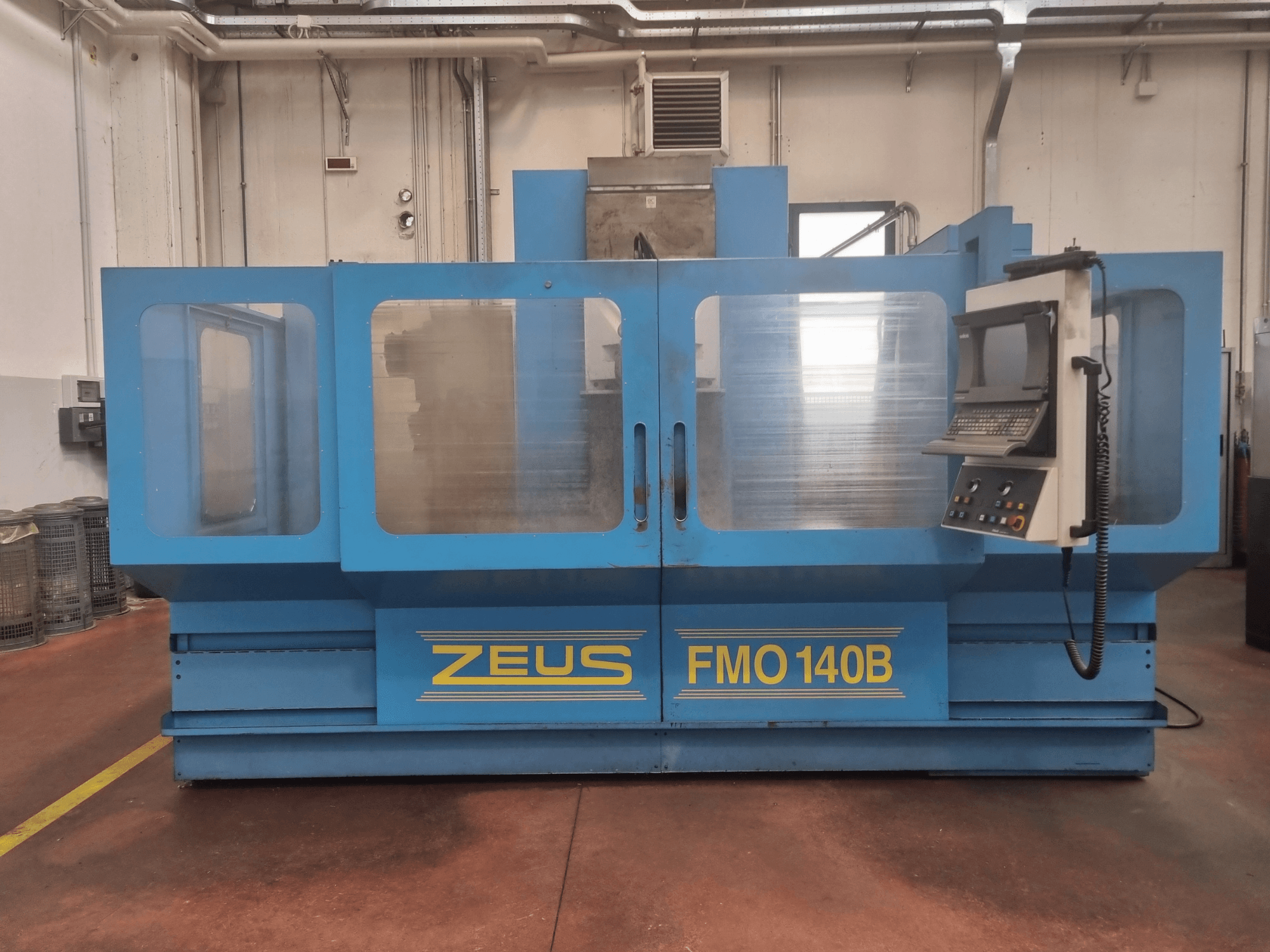 Zeus FMO 140B mašīna zilā krāsā, skats no priekšpuses; ar vadības paneli un lieliem caurspīdīgiem paneļiem redzamībai.