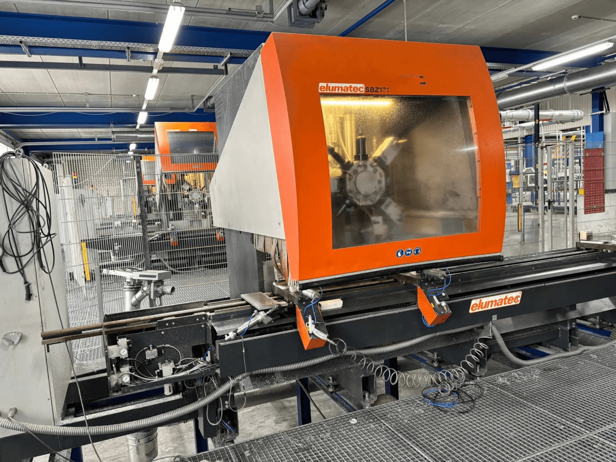 Elumatec SBZ 131 vertikālais apstrādes centrs, priekšējais skats, kurā redzams vadības panelis, mašīnu detaļas un apkārtējā darba vide.