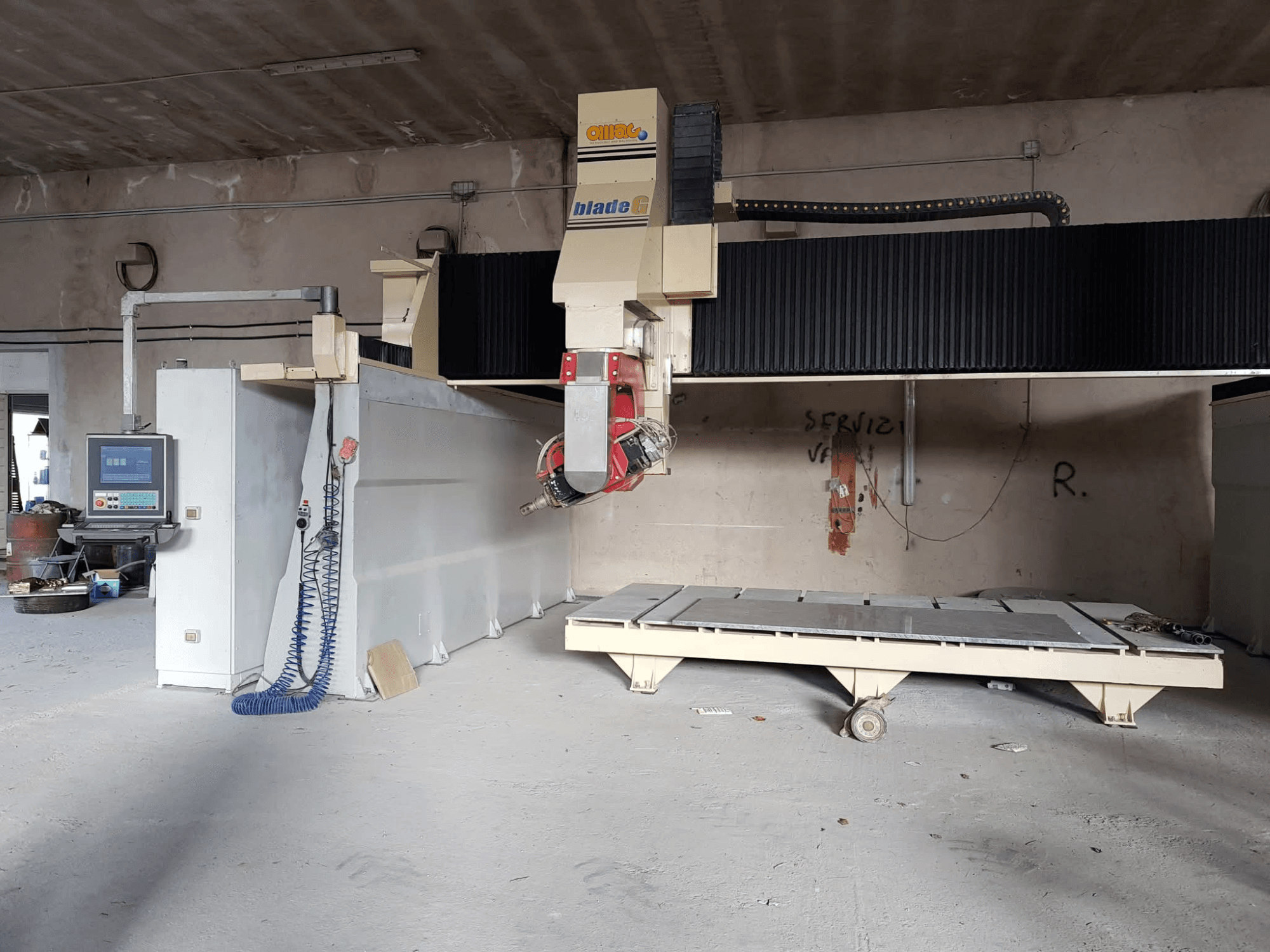 Portālflīzēšanas iekārta OMAG Blade G darbnīcā, skats no priekšpuses, redzams vadības panelis un lielā frēzēšanas gulta.