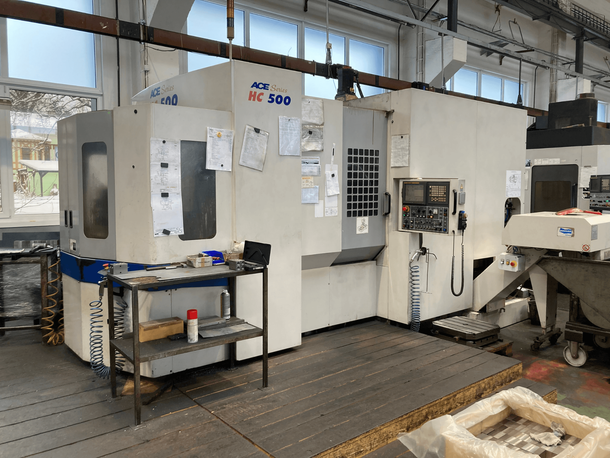 DOOSAN ACE HC-500 horizontālais apstrādes centrs, skats no priekšpuses; ar vadības paneli, vairāku instrumentu uzglabāšanas vietu un industriālo iestatījumu.