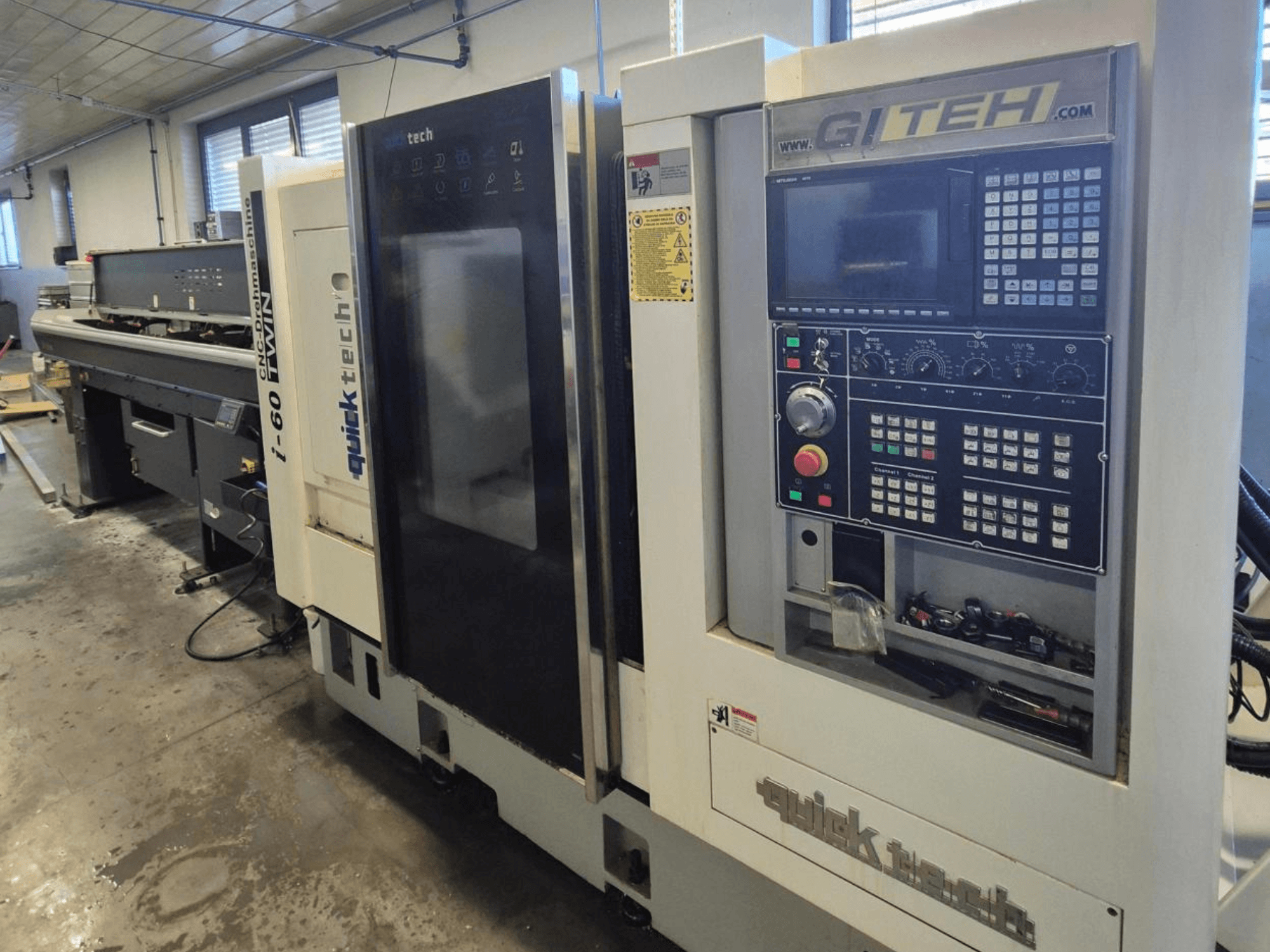 Quick Tech i-60 dvīņu CNC mašīna, skats no priekšpuses, ar GITEH vadības paneli un vadības pogām, darbnīcā.