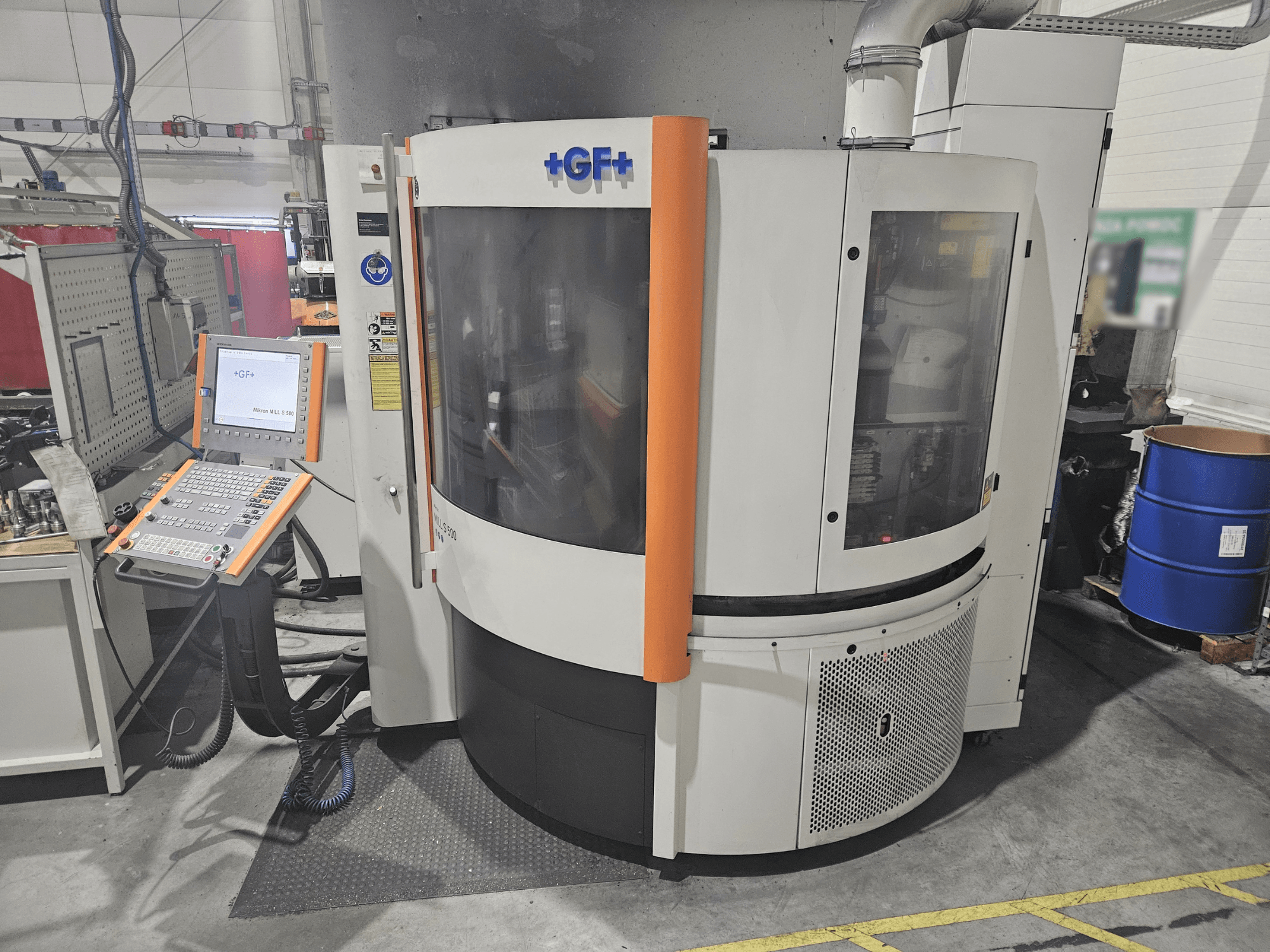 GF Machining Solutions darbagalds ar vadības paneli, skats no priekšpuses; caurspīdīgs panelis, oranži akcenti un rūpnieciski iestatījumi.