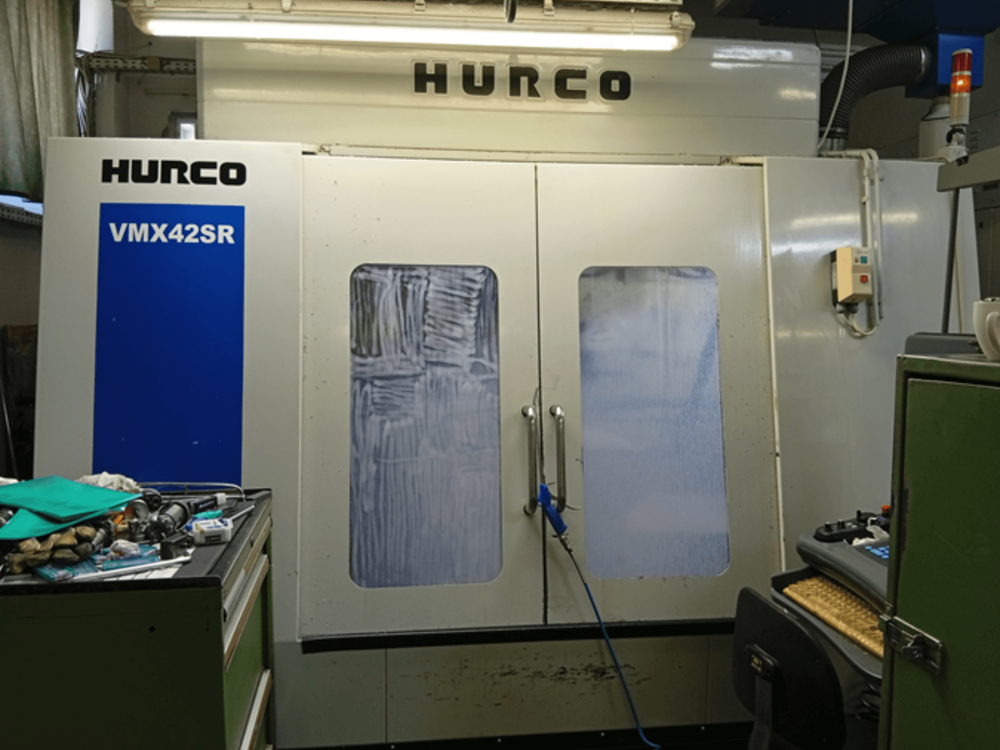 Hurco VMX 42SR vertikālais apstrādes centrs priekšpusē, ar zilu paneli, vadības saskarni un tīru darba telpu.