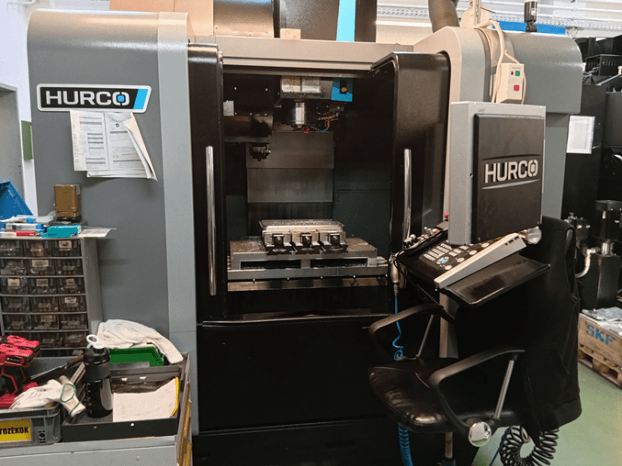 Hurco VMX 30i vertikālais apstrādes centrs priekšpusē, ar vadības paneli, darba galdu un darba iestatījumiem.