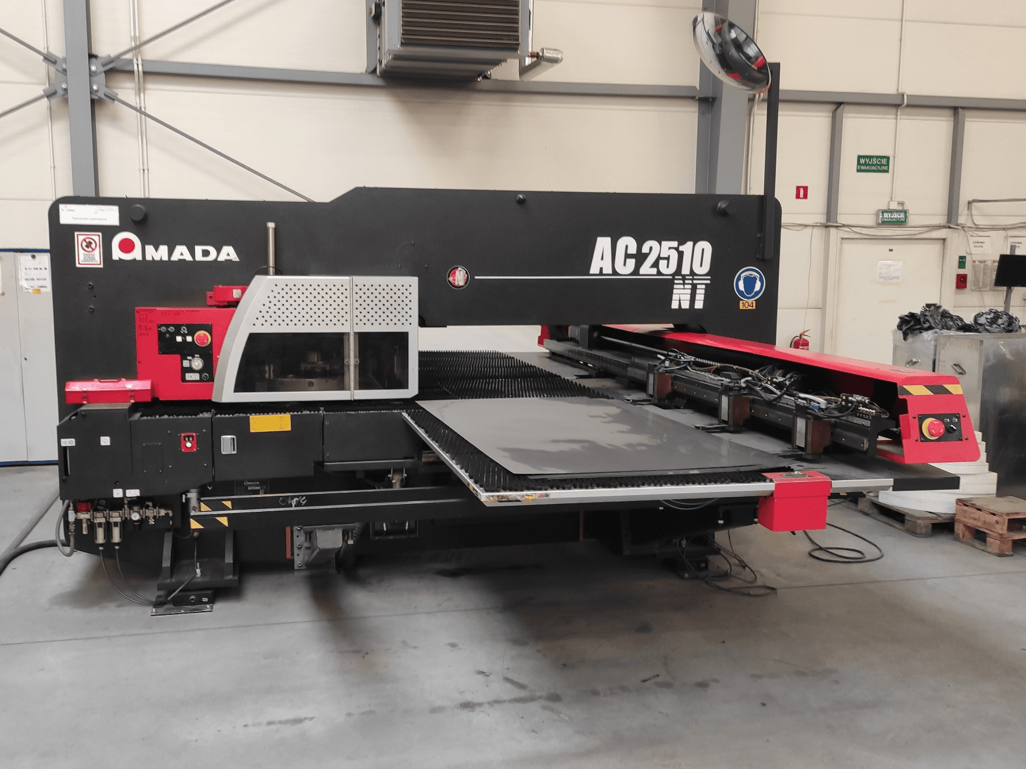 Amada AC2510 NT CNC caurumošanas iekārta, skats no priekšpuses, ar vadības paneli un lokšņu iekraušanas zonu.
