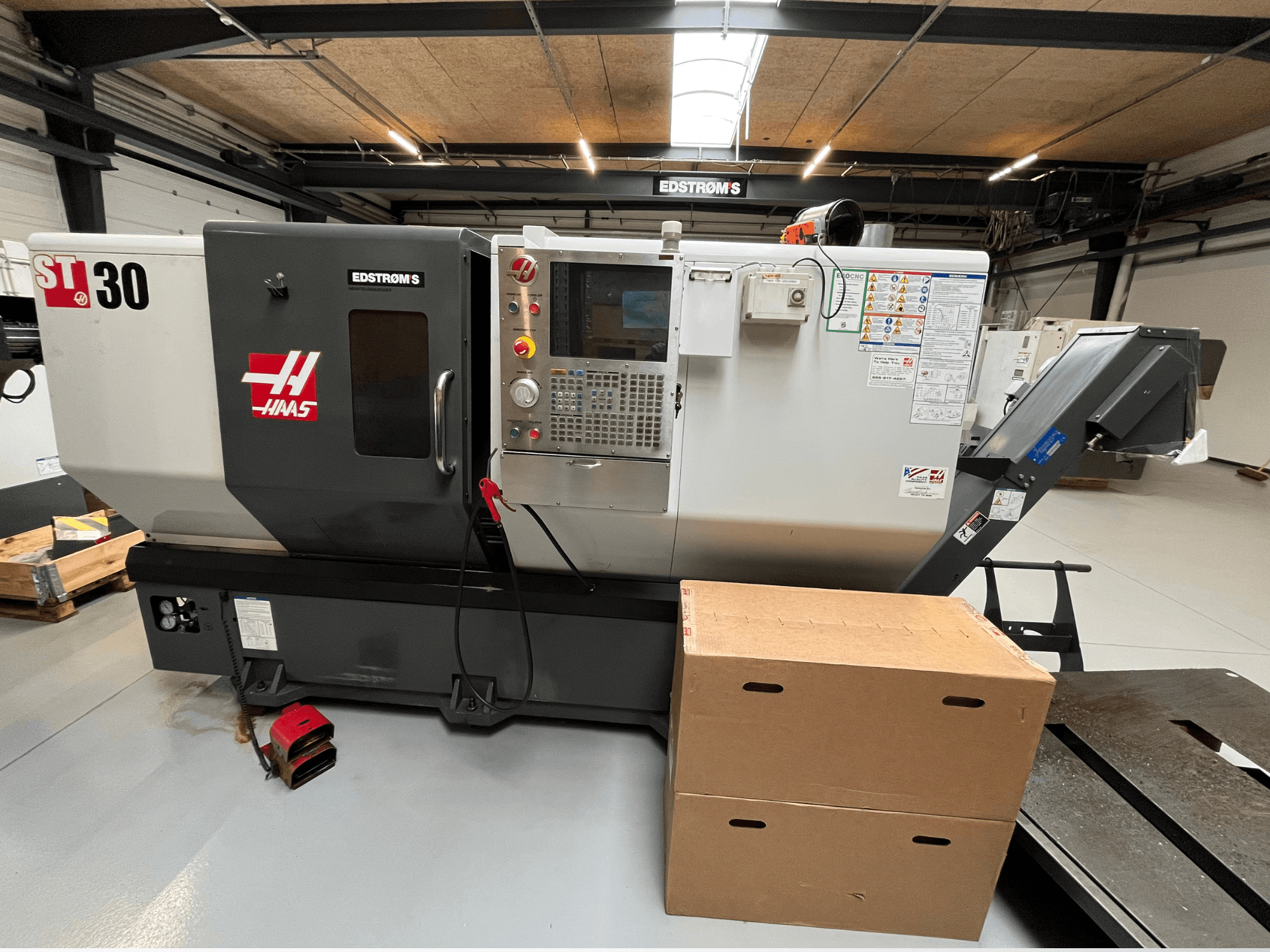 Haas ST-30 CNC virpa, skatoties no sāniem, ar vadības paneli, modeļa nozīmīti un divām kartona kastēm blakus.