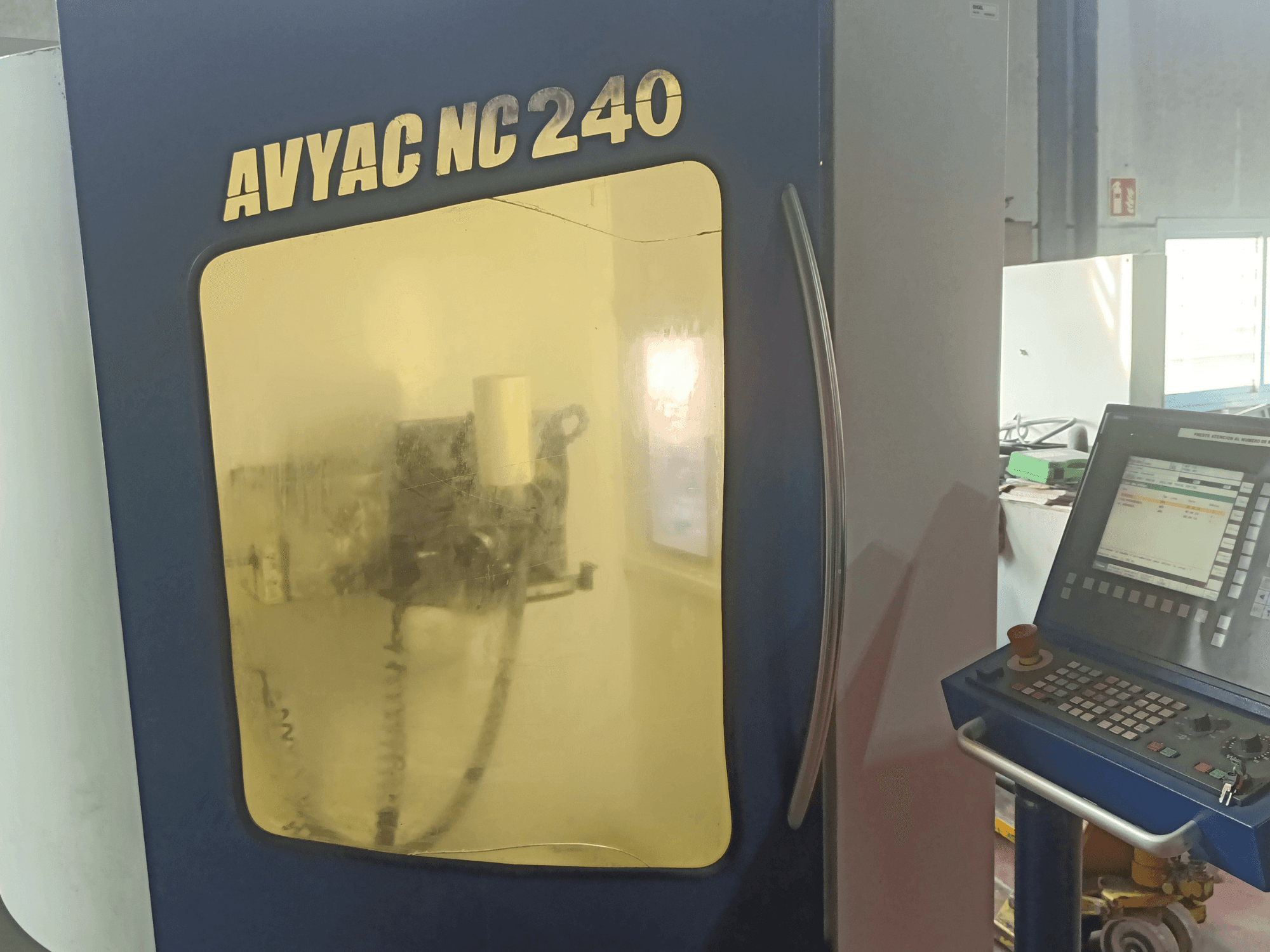 AVYAC NC240 cilindriskās slīpmašīnas, sānu skats, kurā redzams vadības panelis un daļēji caur logu redzamā slīpēšanas zona.