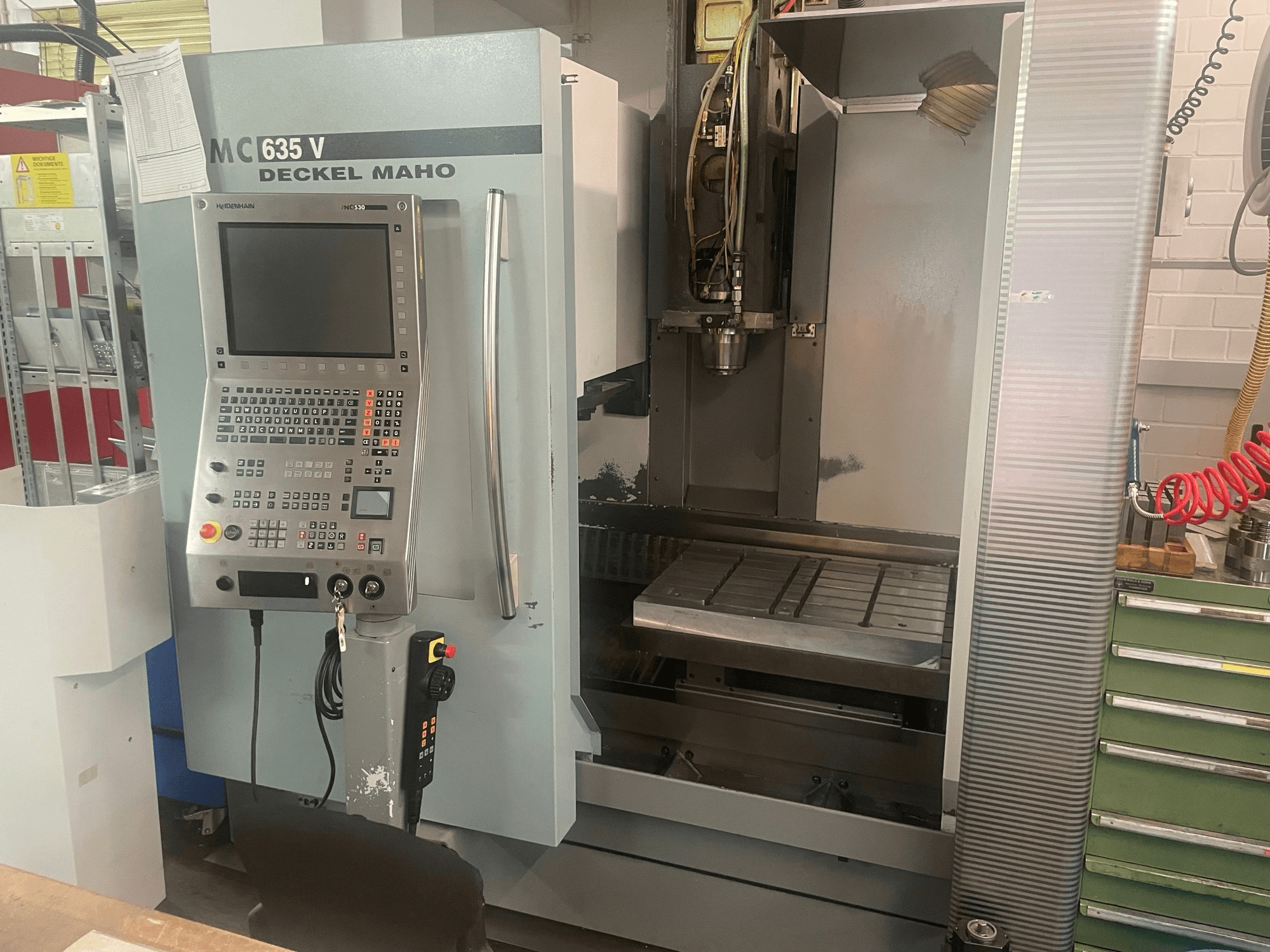 DECKEL MAHO DMC 635 V vertikālā apstrādes centra skats no priekšpuses ar vadības paneli un atvērtu darba zonu, kurā redzama instrumentu galva un galds.
