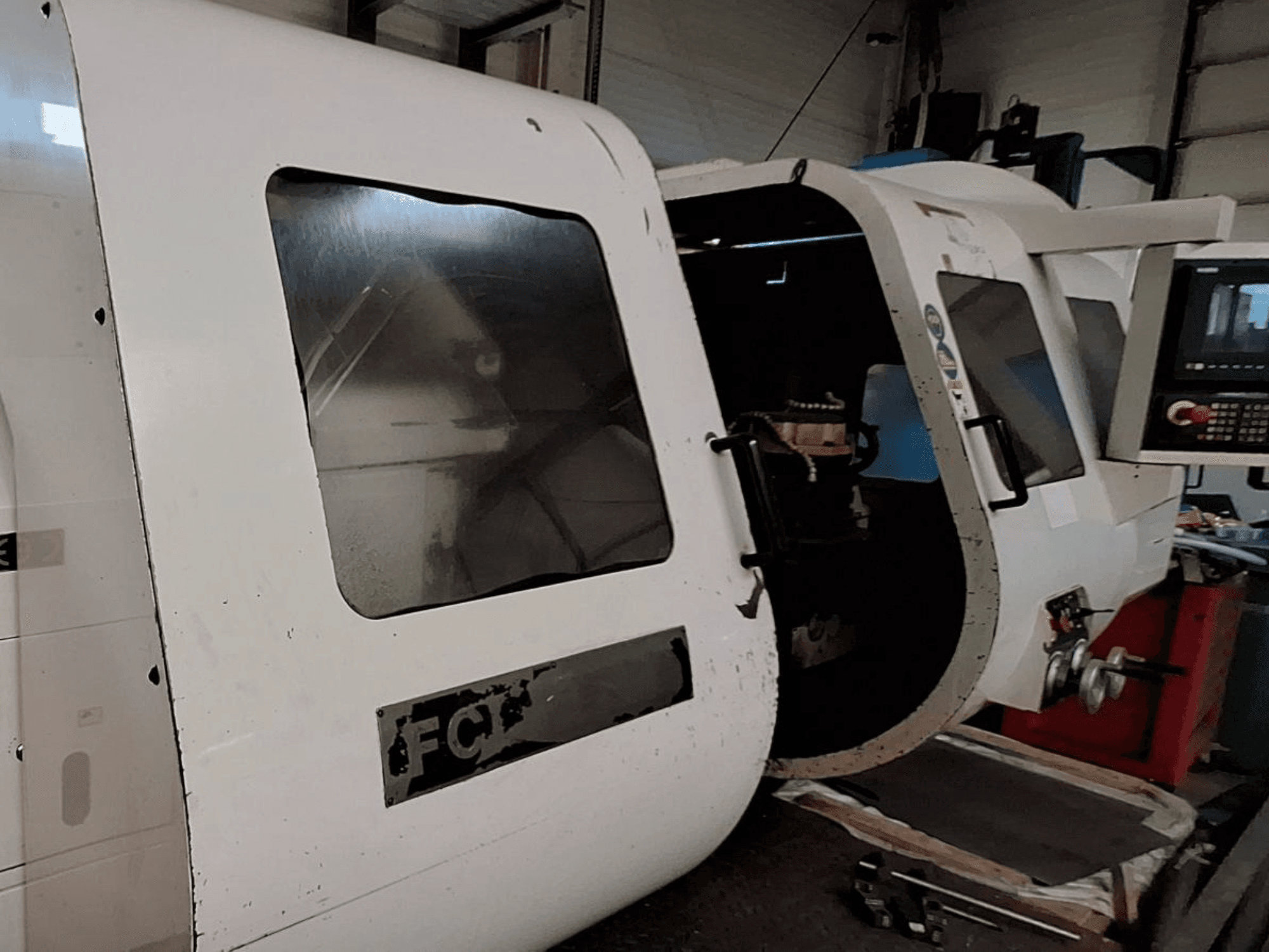 Balta CNC iekārta ar redzamu vadības paneli un atvērtām durvīm, kas parāda iekšējās sastāvdaļas; skats no priekšpuses. Zīmols: FCT.