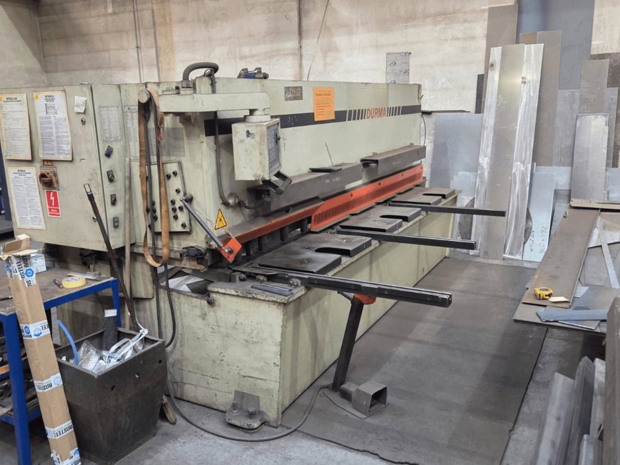 Hidrauliskās šķēres Durma SB 3060, skats no priekšpuses, redzamas vadības ierīces, griešanas asmens un metāla loksnes darba zonā.