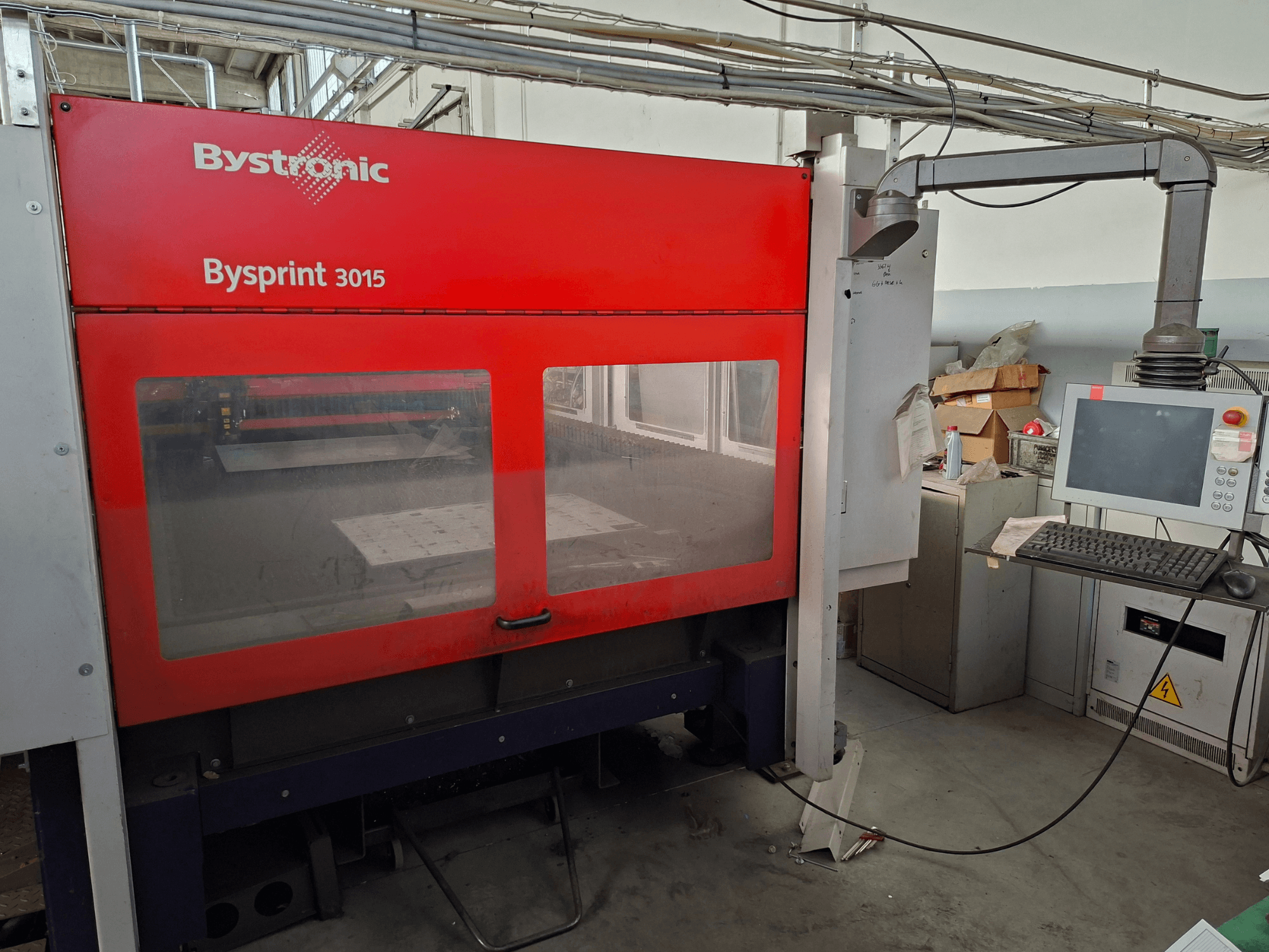 „Bystronic Bysprint 3015“ CO₂ lāzergriešanas iekārta, skats no priekšpuses, kurā redzams vadības panelis un lāzergriešanas zona.