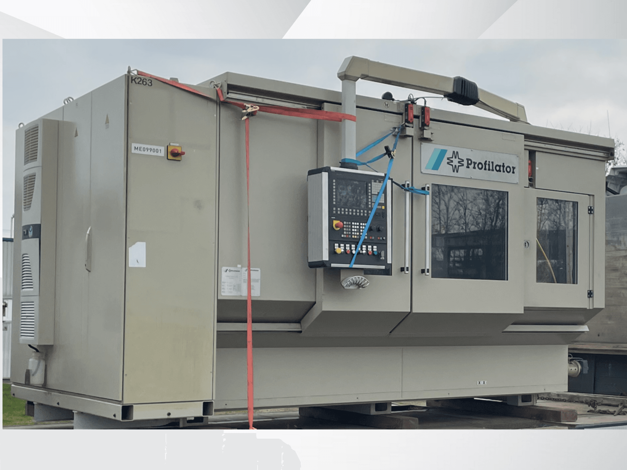 Profilēšanas iekārta sānu skatā, ar vadības paneli, drošības marķējumu un aizsargplākšņiem uz koka platformas.