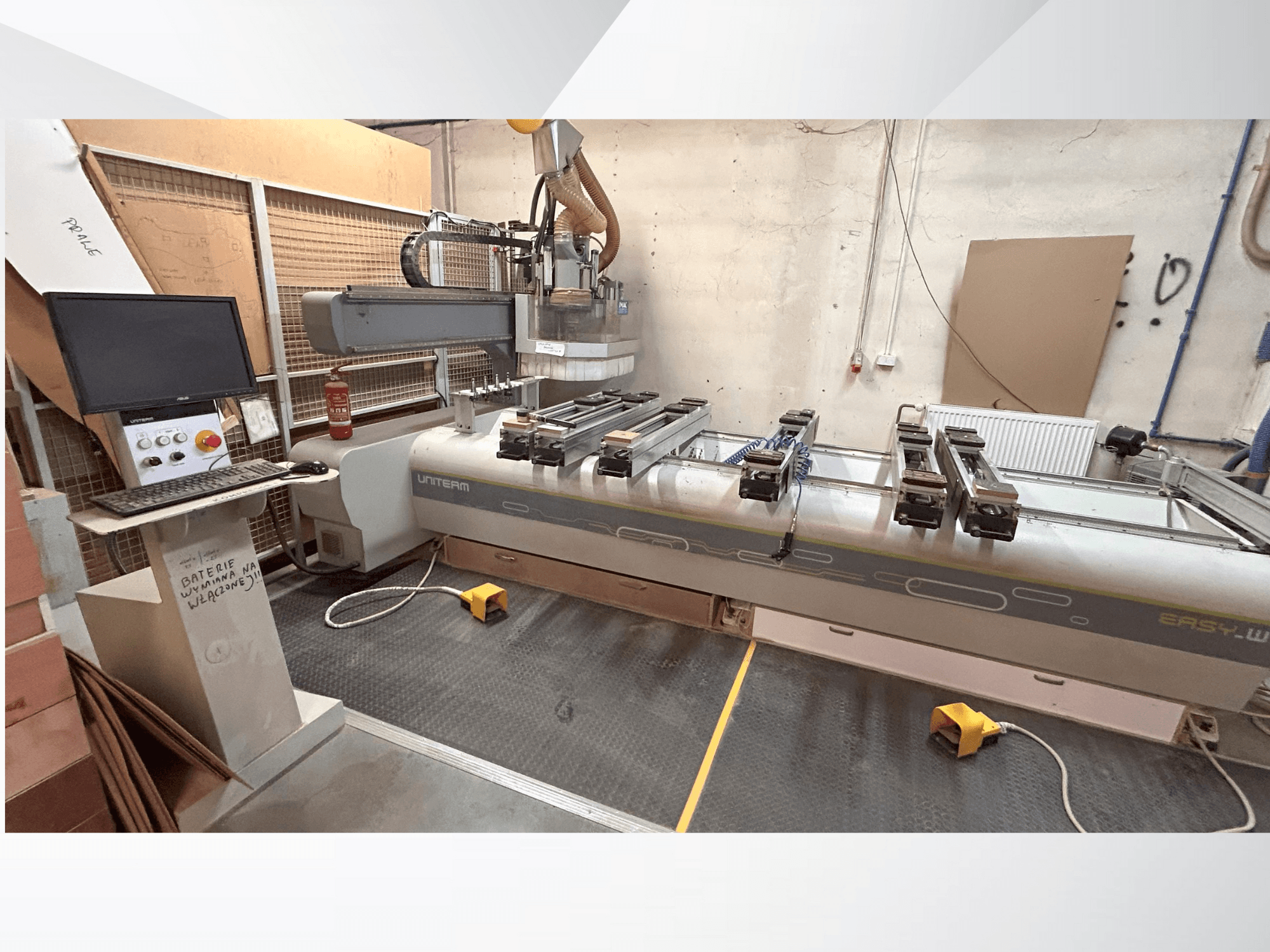 UNITEM EASY-W CNC mašīnas priekšējais skats ar vadības paneli, monitoru un piestiprinātiem apstrādājamiem priekšmetiem uz darba galda.