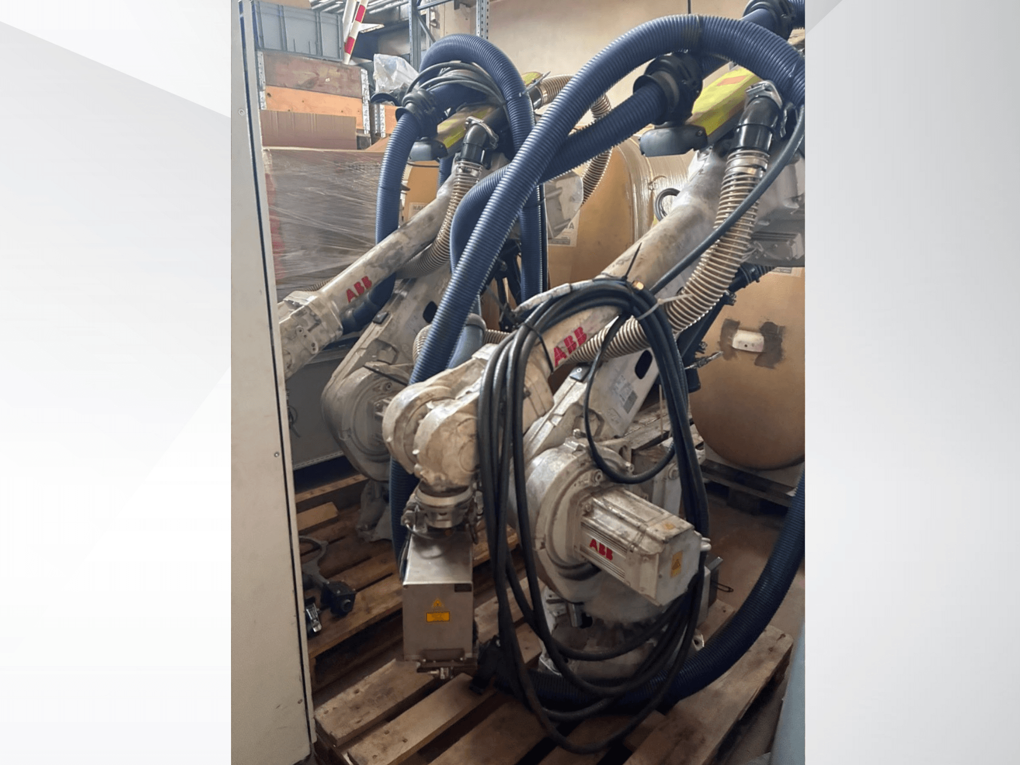 ABB IRB 4600-40/2.55 robota roka, sānskats, kurā redzamas divas rokas un pievienotās šļūtenes; uzstādīta uz paliktņiem noliktavas vidē.