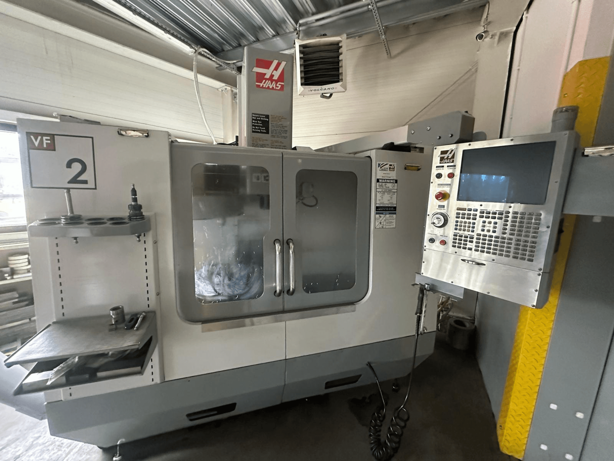 Haas VF-2 CNC darbgalds, skats no priekšpuses, ar vadības ierīcēm, instrumentu turētāju un caurspīdīgām durvīm ar redzamiem instrumentiem korpusa iekšpusē.