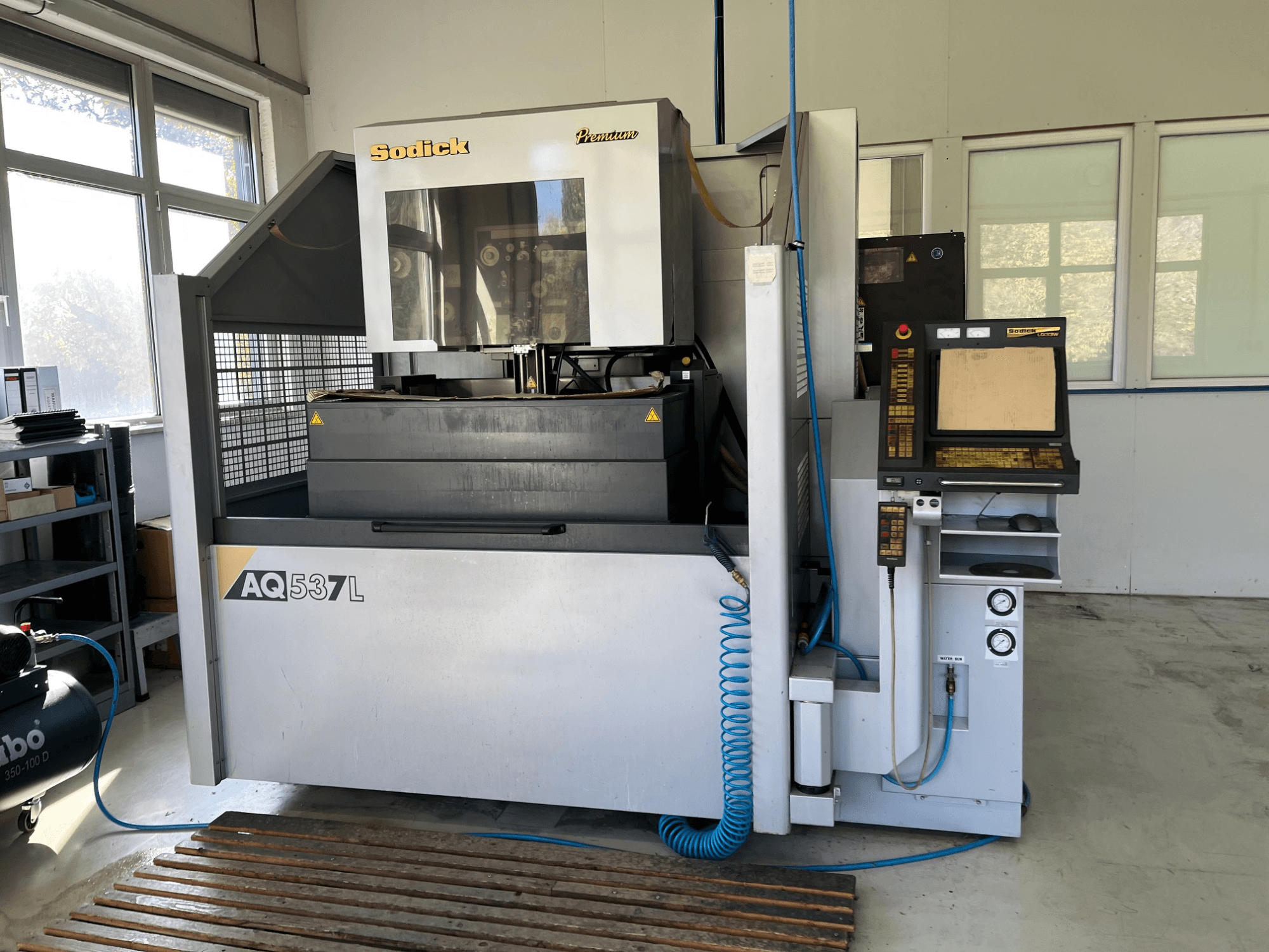 Sodick AQ537L elektriskās izlādes mašīnas (EDM) priekšējais skats, ar vadības paneli, ūdens dzesēšanas līnijām un darba vietu.