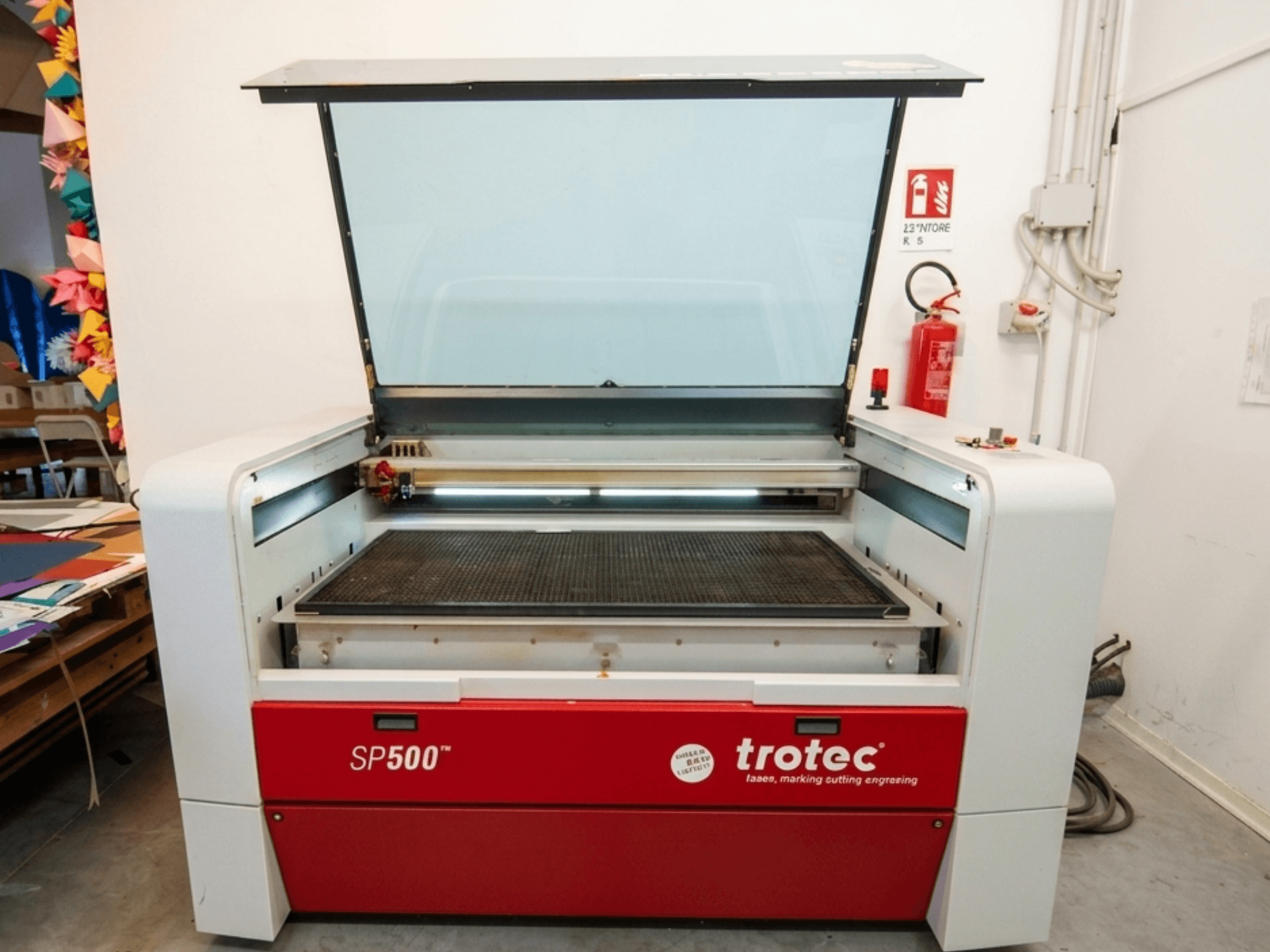 Trotec SP500 C200 lāzergravēšanas iekārta priekšpusē ar atvērtu vāku, kurā redzama darba zona un vadības ierīces.