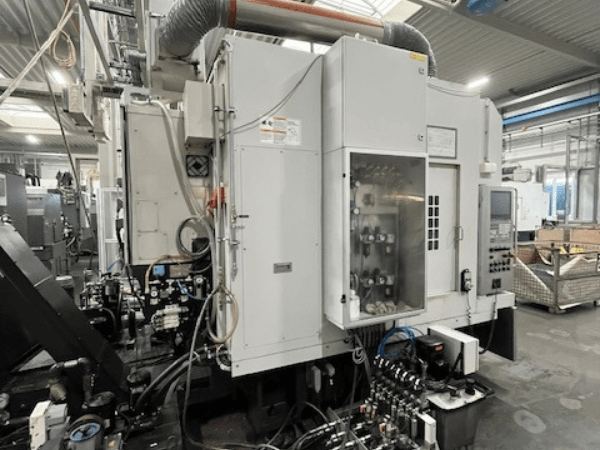 Rūpnieciskās mašīnas sānu skats, kurā redzams vadības panelis un hidrauliskie komponenti, kā arī zīmola un modeļa detaļas.