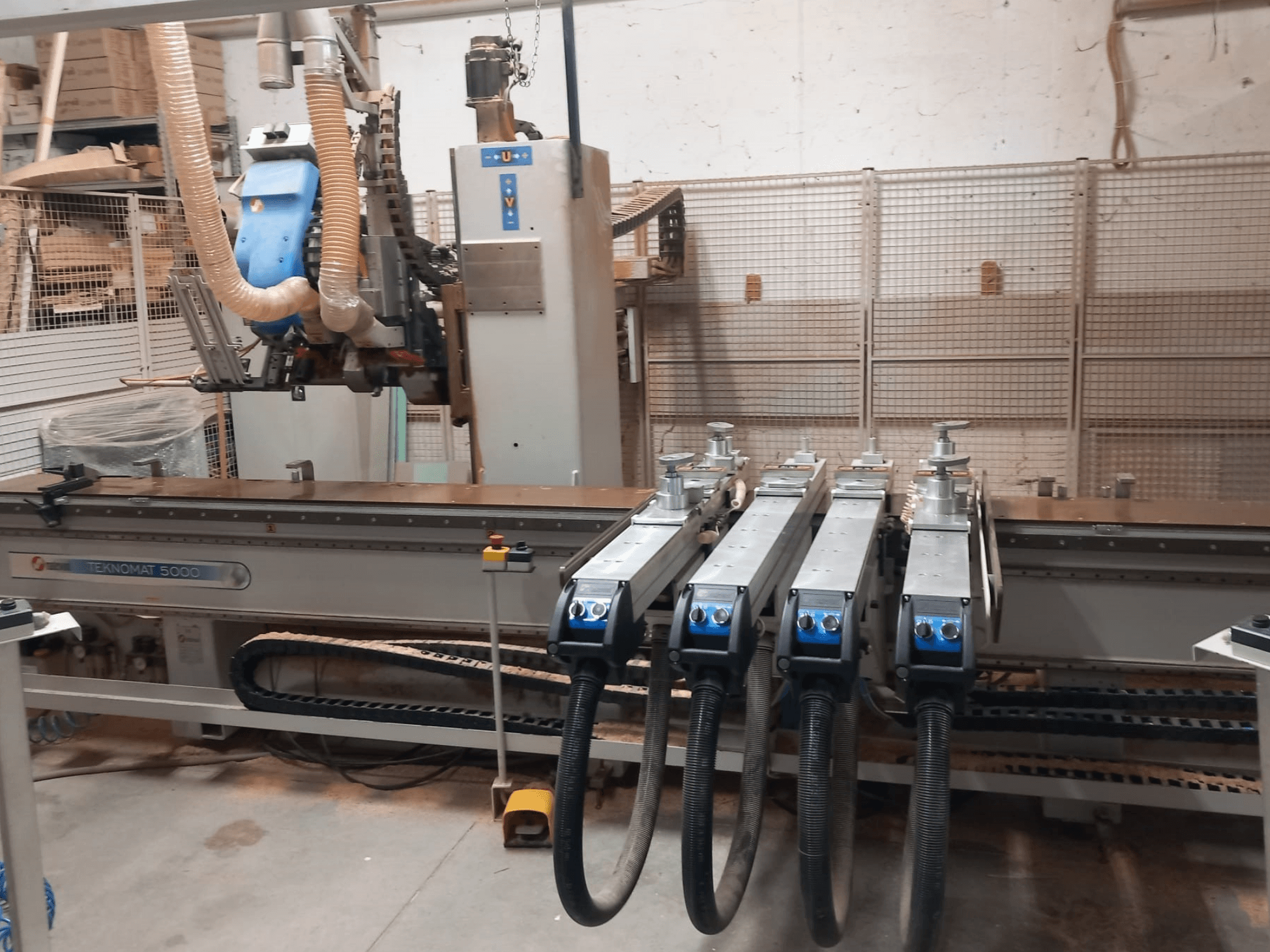 CNC koka apstrādes centrs MASTERWOOD TEKNOMAT 5000, skats no priekšpuses, kurā redzama instrumentu galva un vairākas nosūces šļūtenes.