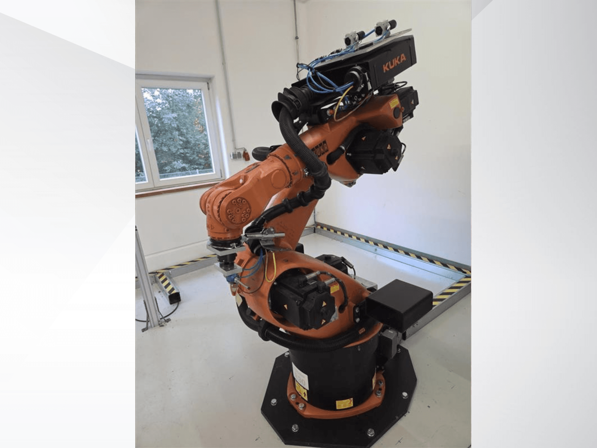KUKA KR60 HA robota roka no sāniem, kurā redzami mehāniskie savienojumi un vadu izvietojums uz rūpnieciskā pamatnes.