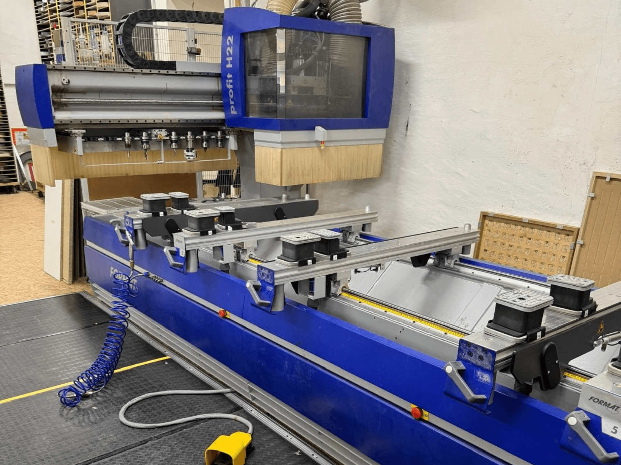 FORMAT4 PROFIT H22 CNC koka apstrādes centrs, skats no priekšpuses, uz zilā korpusa redzami apstrādes rīki un fiksatori.
