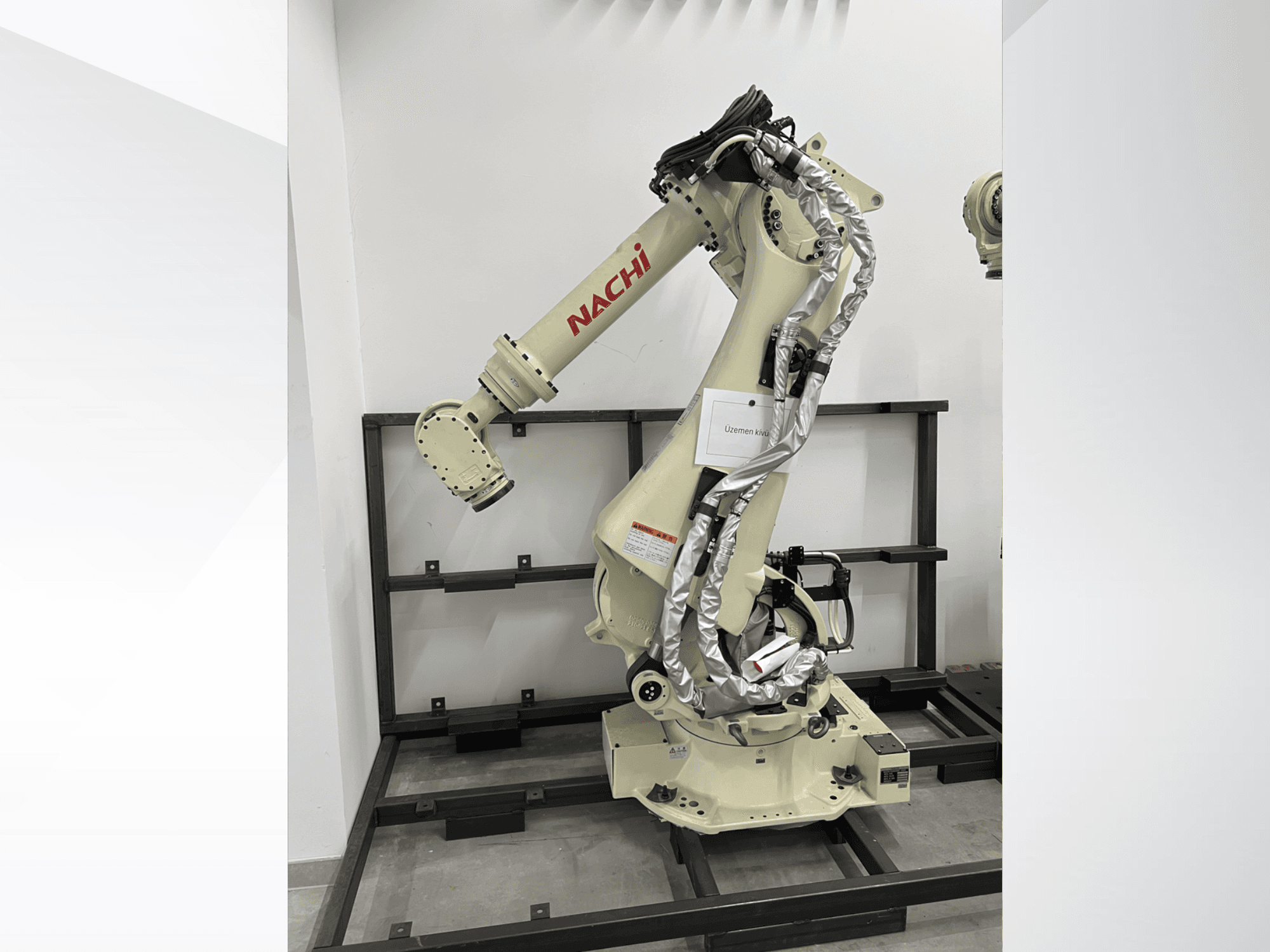 NACHI SRA166-01 robota roka sānu skatā, ar lokanām locītavām, pievienotiem kabeļiem un uzstādīta uz aizsargrāmja.