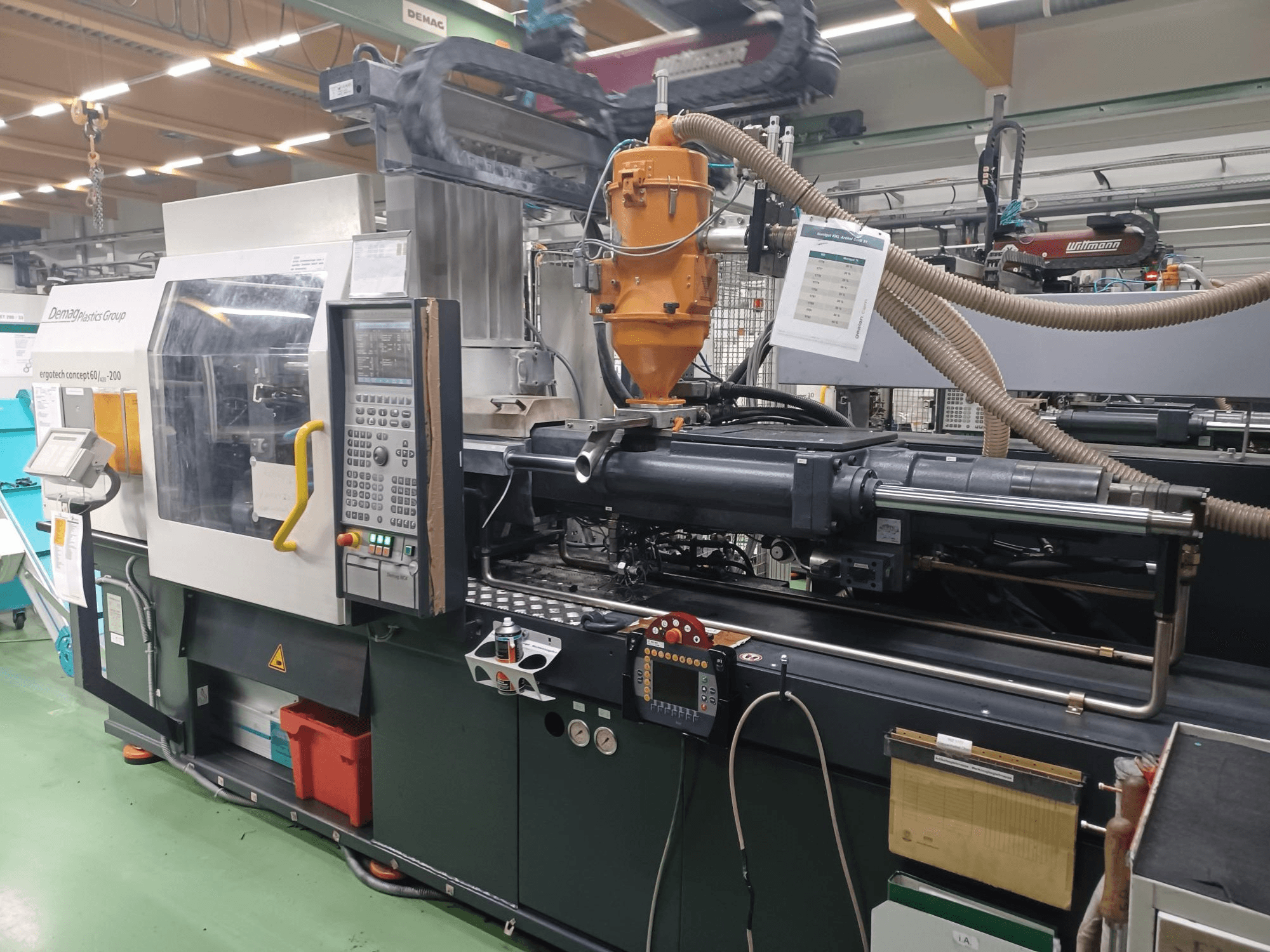 Demag Ergotech 200 injekcijas formēšanas iekārta, skats no priekšpuses, redzams vadības panelis, sprausla un darbības komponenti.