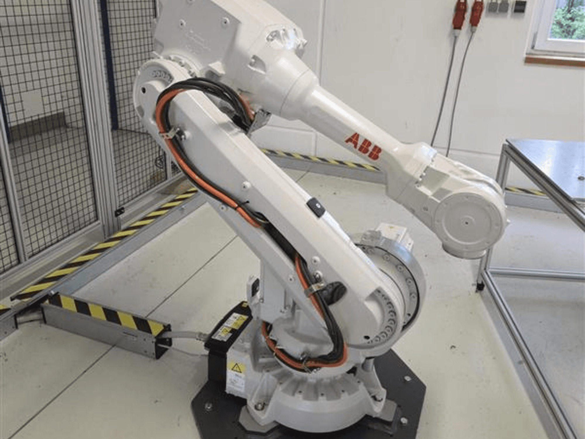 ABB IRB 4600-45/2.05 robota roka profilā, kurā redzama tās šarnīrveida konstrukcija un pie pamatnes pievienotie kabeļi.